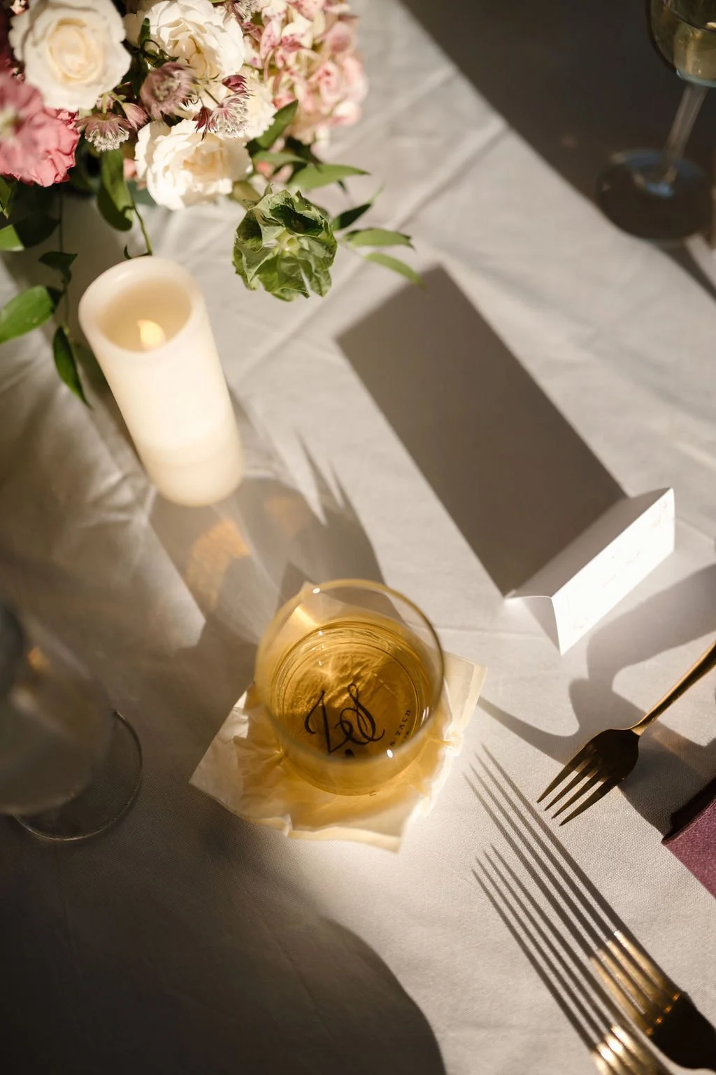 Monogrammed whiskey glass beside a pillar candle and gold flatware in warm light, a detail from one of the Fort Wayne wedding venues