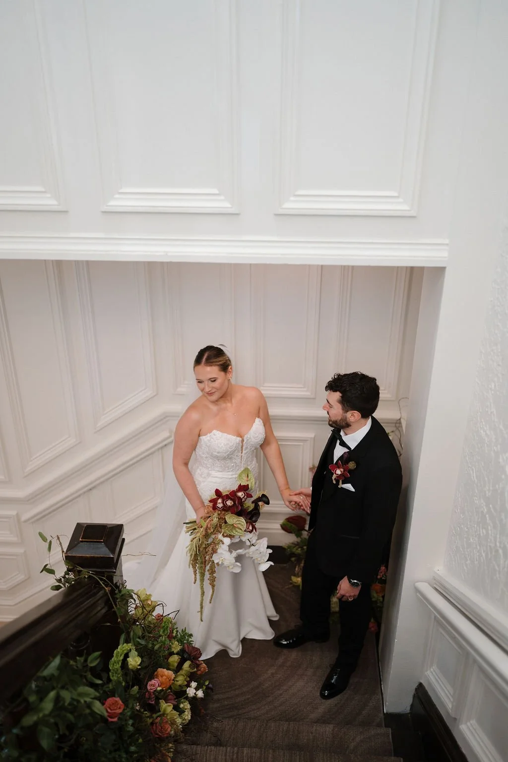 Bride and groom holding hands on a floral-lined staircase, shot from above, at one of the elegant Fort Wayne wedding venues