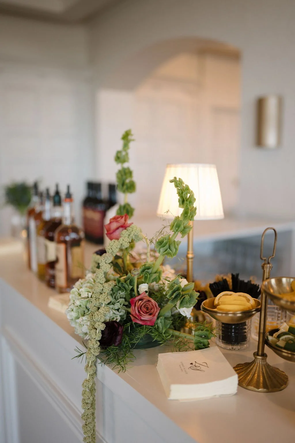 Reception bar styled with bells of Ireland, hydrangea, and roses, plus a gold fruit stand and monogrammed napkins at one of the Fort Wayne wedding venues