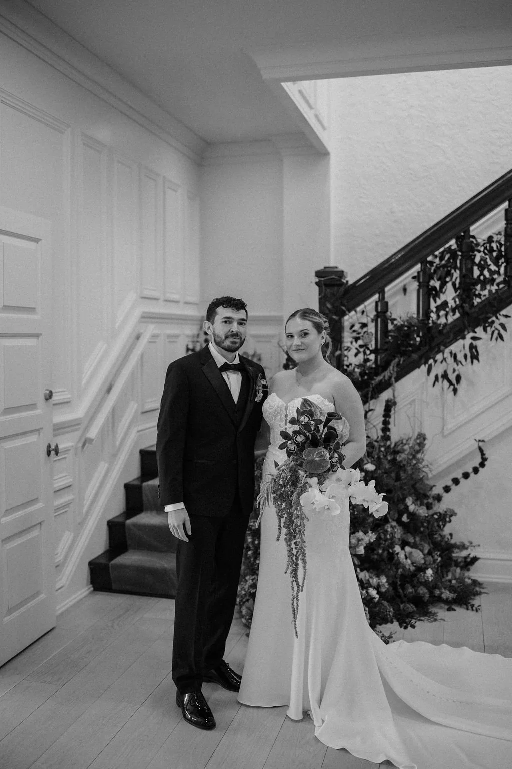 Black and white portrait of a bride and groom at the base of a floral staircase in one of the Fort Wayne wedding venues