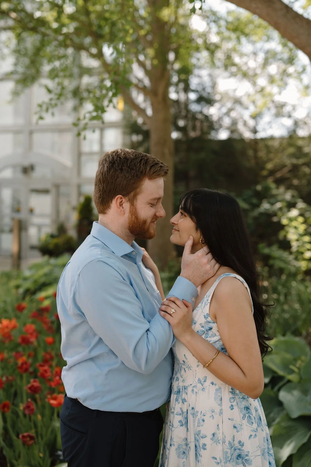 Engagement photo ideas for a close and romantic pose, with a couple smiling as they look at each other beside red tulips in a garden.