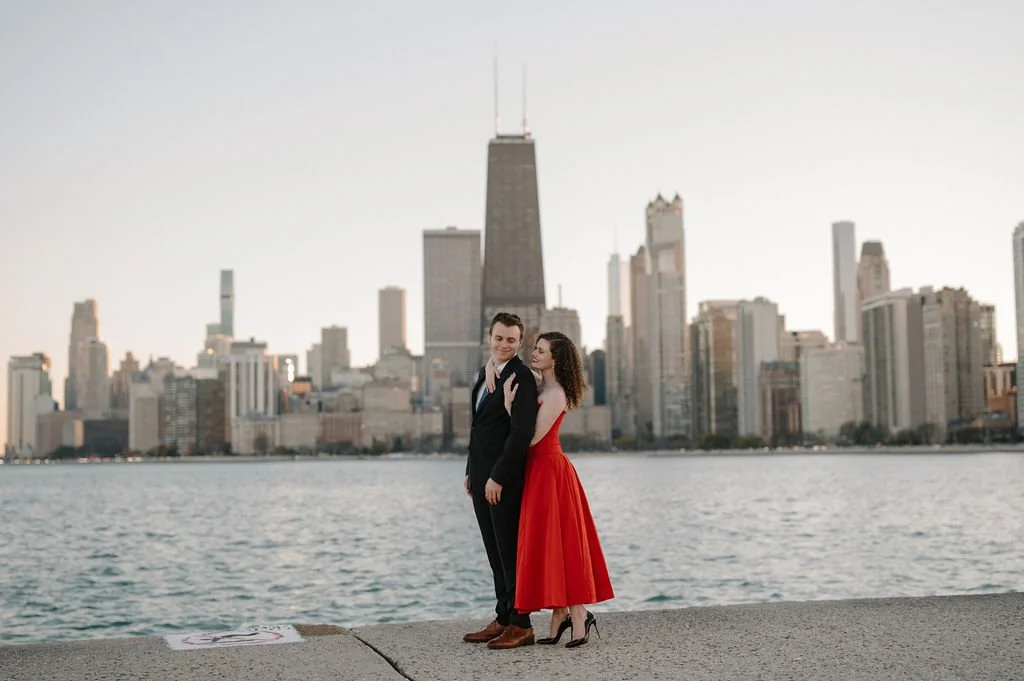 Chicago engagement photos on the lakefront, with a woman in red wrapping her arms around her fiancé, skyline behind them
