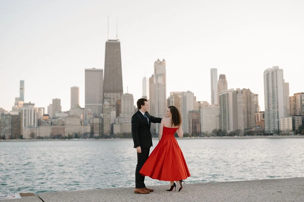 Chicago engagement photos on the lakefront, with a man twirling his fiancée in a red dress in front of the skyline