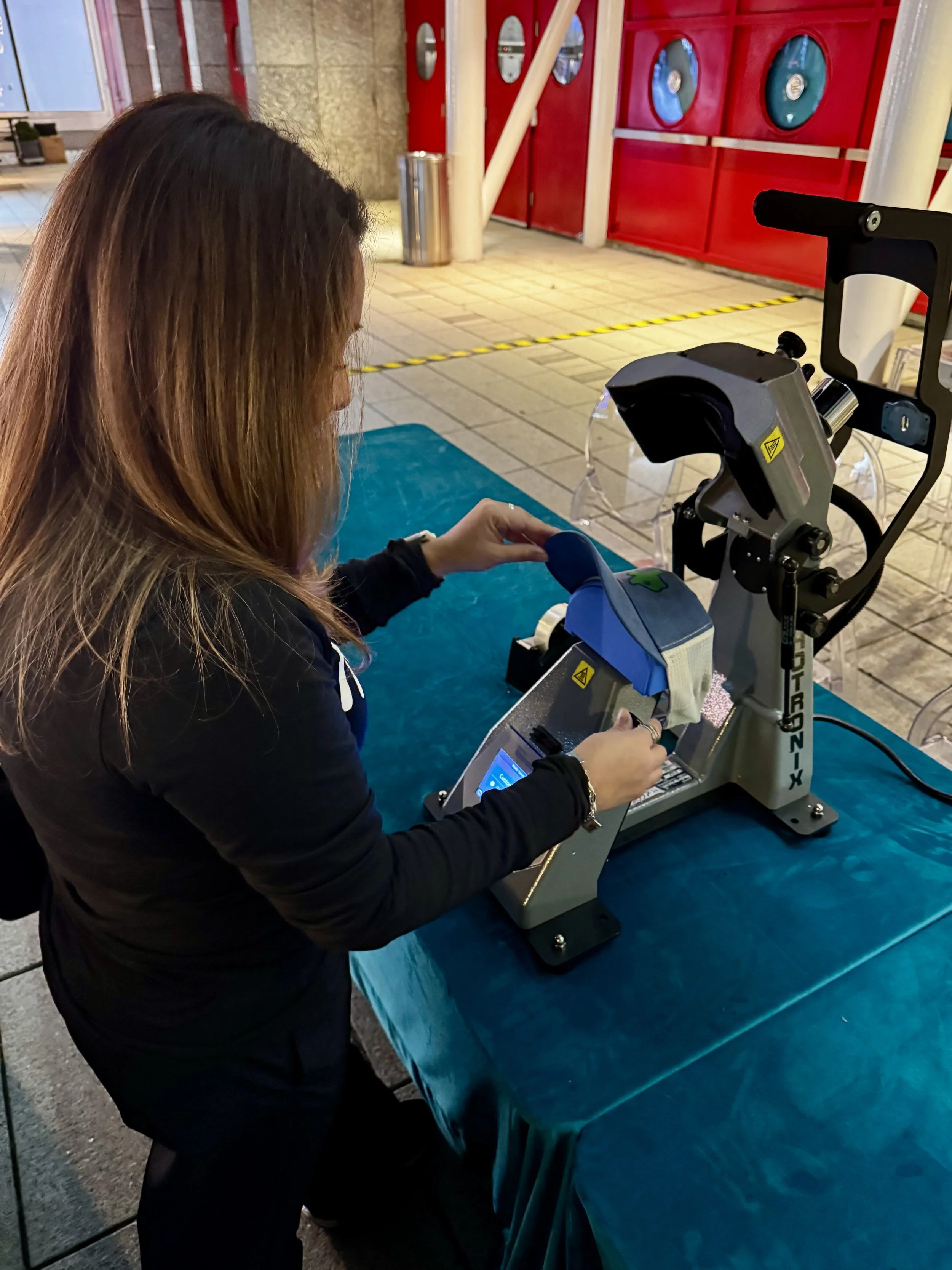 apdat staff fit hat onto heat press to apply woven patches made custom for houston first launch party at expo expo