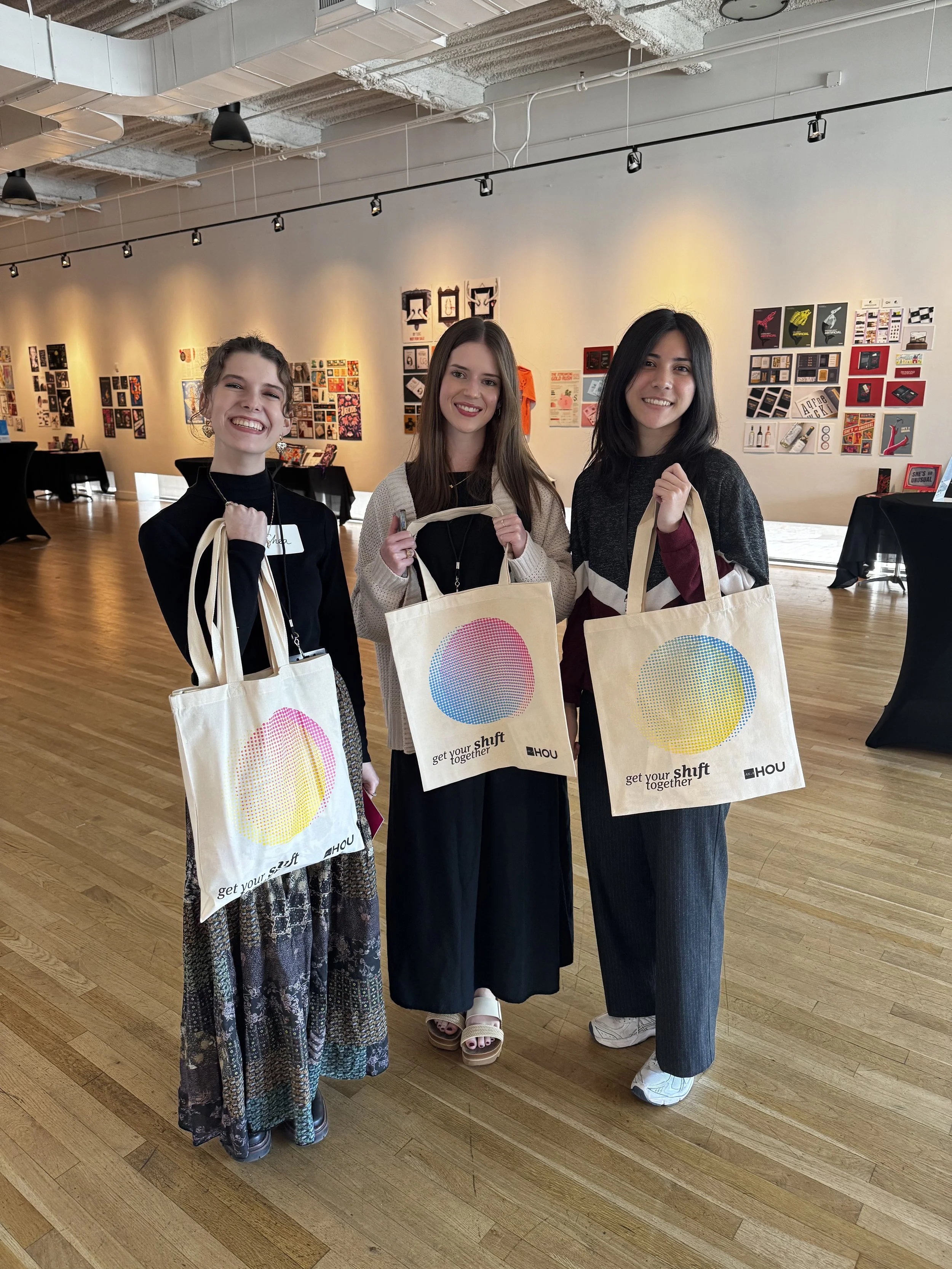 Three AIGA Symposium attendees model their hot of the press tote bags at APDAT print co's screen printing booth