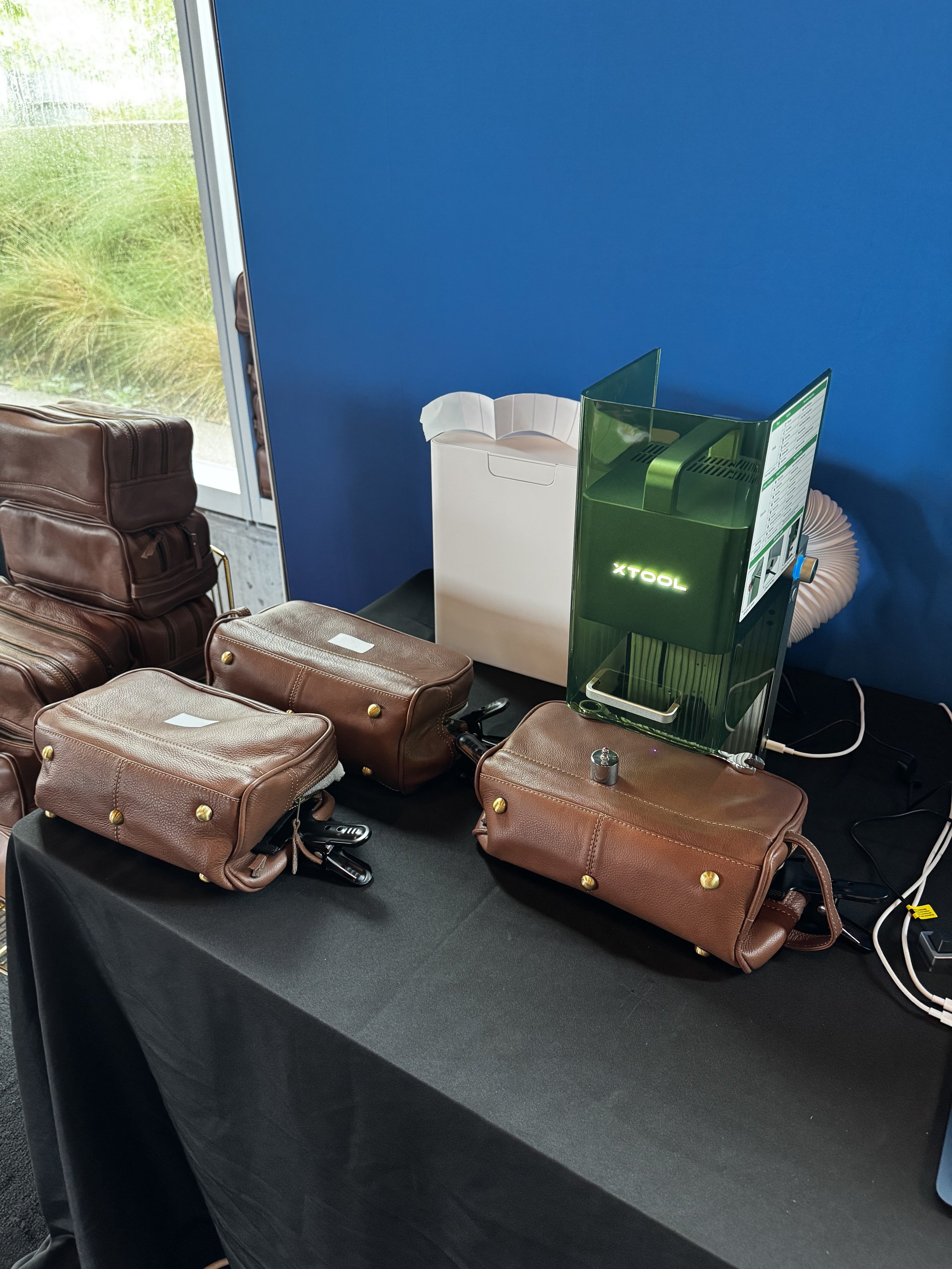 Set up including leather dopp kits that have been clamped and weighted down to provide flat surface for live laser engraving