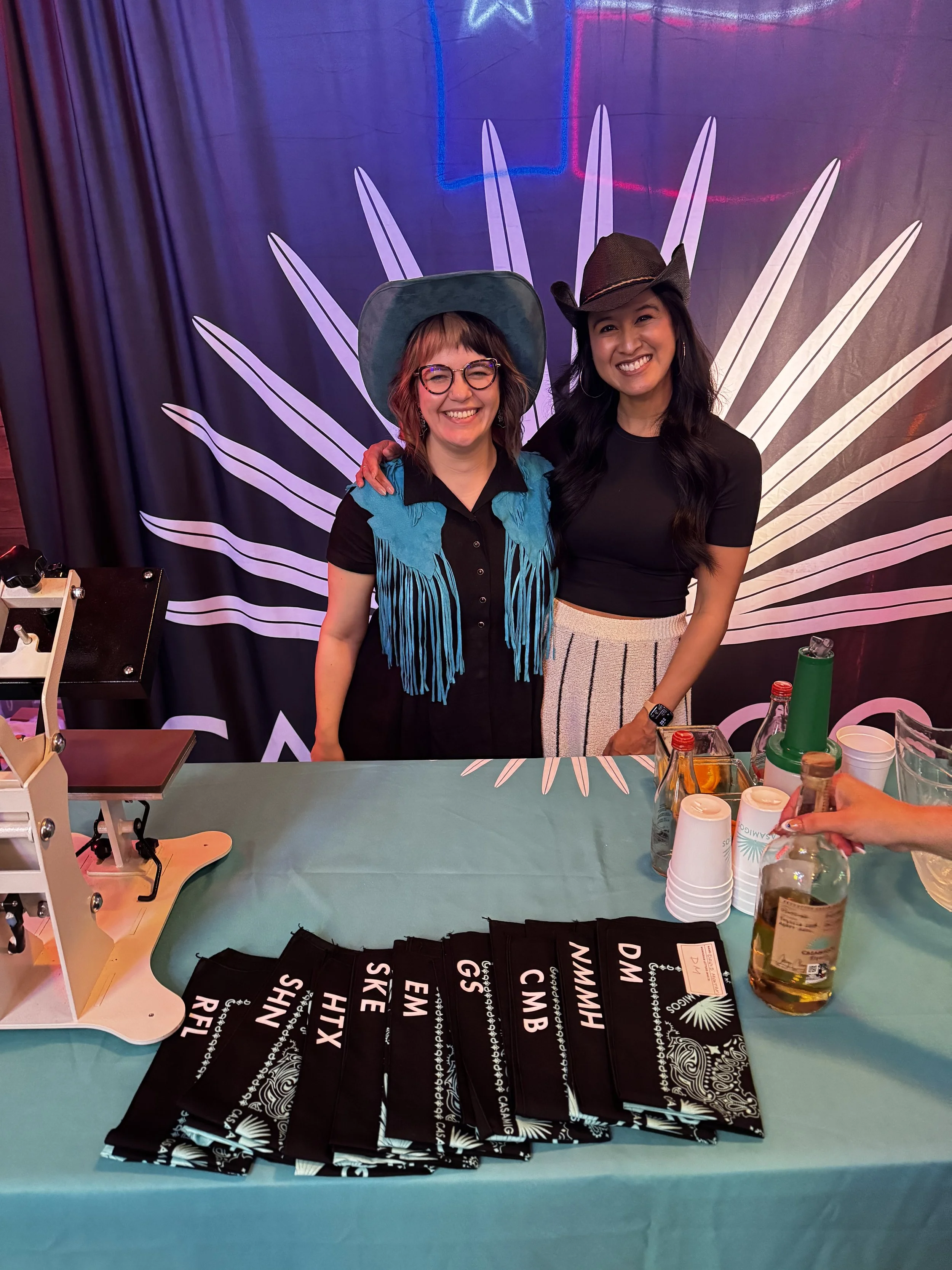 Apdat staff cheesing in front of completed guest bandanas monogrammed live on site