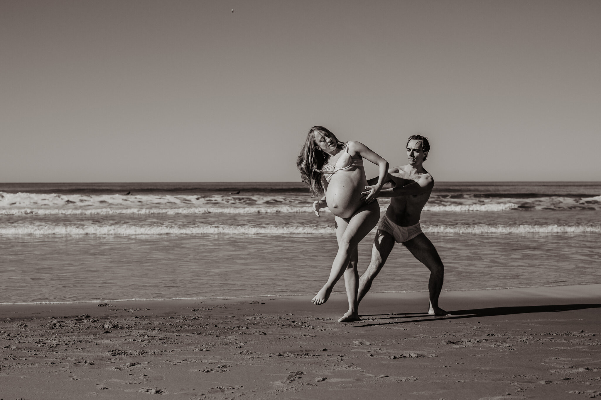 Pregnant woman dancing with partner on beach