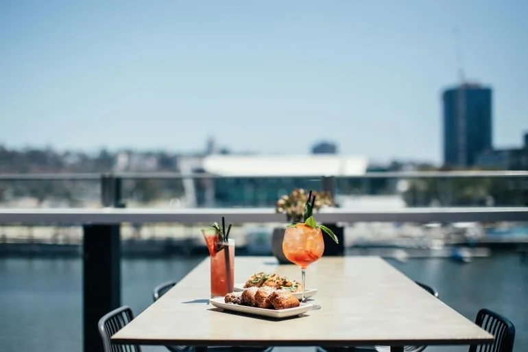 Rooftop table with cocktails and appetizers overlooking the Seattle waterfront on a clear day.