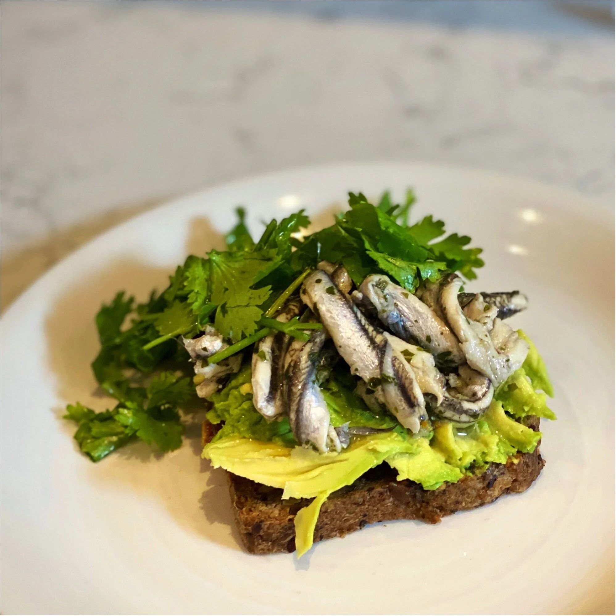 Gluten and wheat free nut toast with mashed avocado and sardines, lemon and coriander