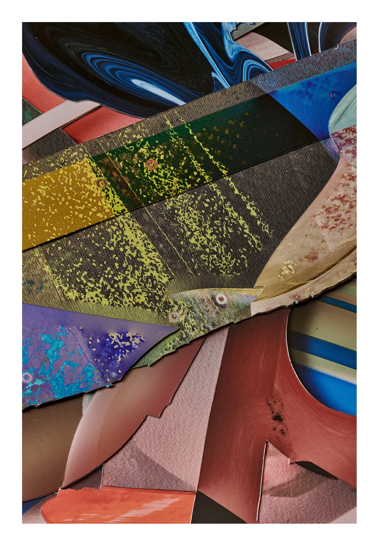 Close-up image of various colored, metallic, and textured paper or cardboard pieces layered together, resembling an abstract art composition.