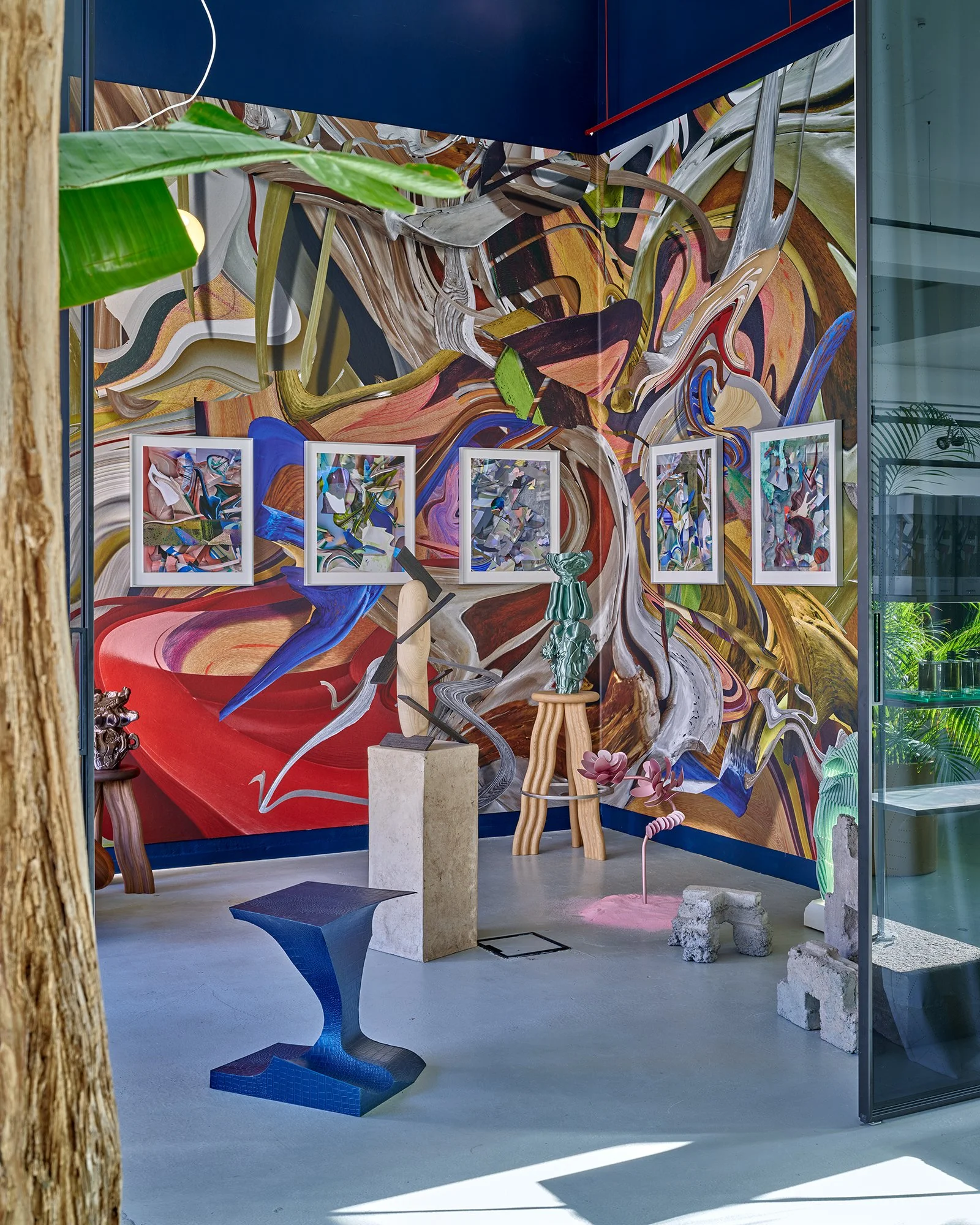 An art gallery display featuring abstract and colorful paintings on a wall and various sculptural pieces and furniture in the room.