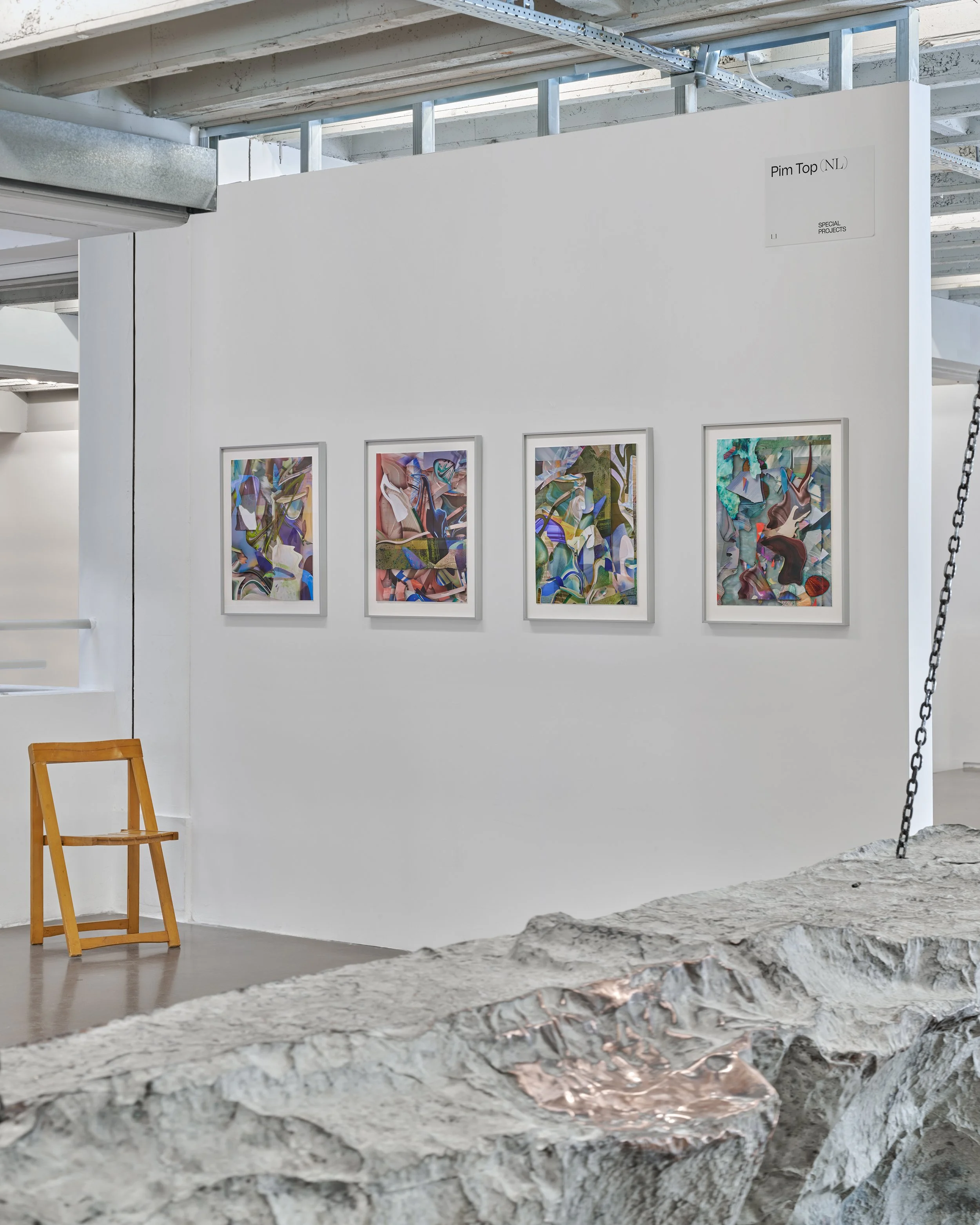 An art gallery with abstract paintings on white walls, a wooden chair, and a rough stone floor.