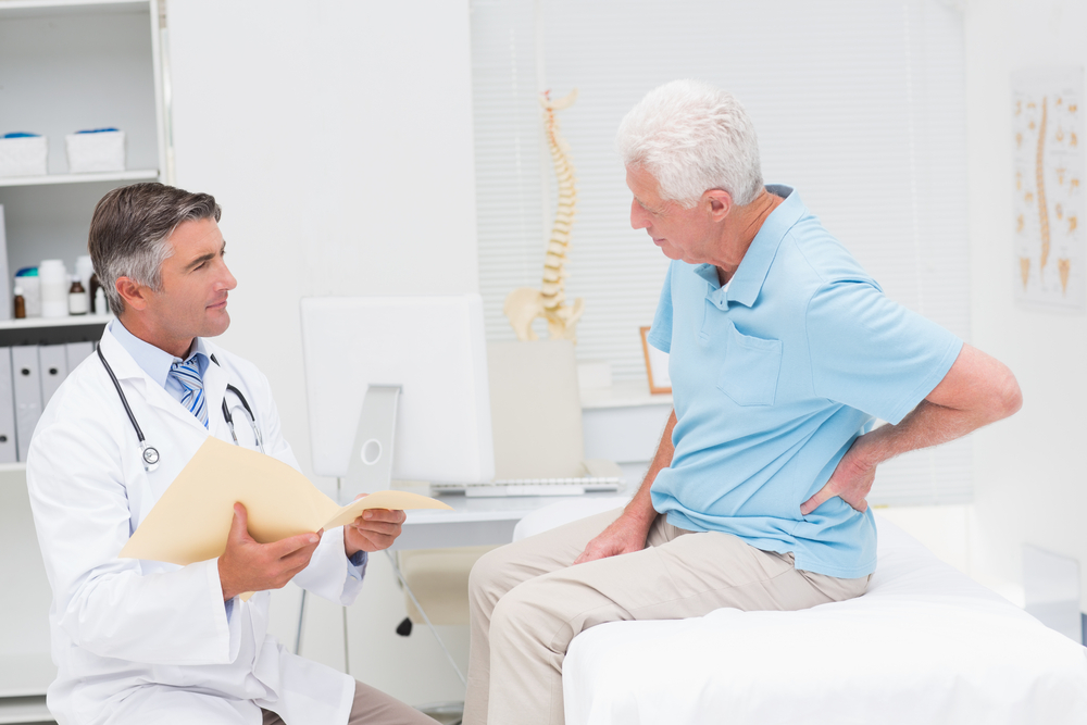 Male doctor discussing reports with senior patient suffering from back pain in clinic.jpg