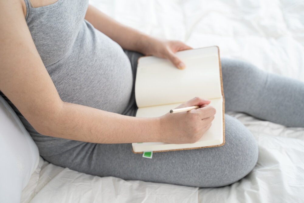 Pregnant woman makes notes in notebook. pregnancy, parenthood, preparation and expectation concept.