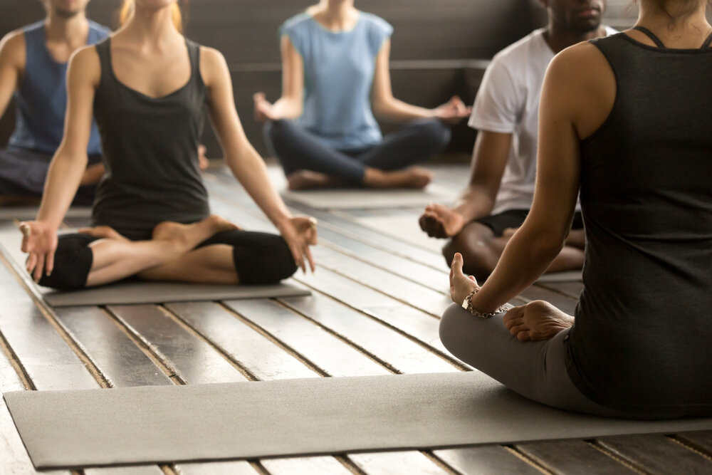 Group of young sporty people practicing yoga lesson with instructor, sitting in Sukhasana exercise, Easy Seat pose, working out, students training in sport club, studio close up, back view