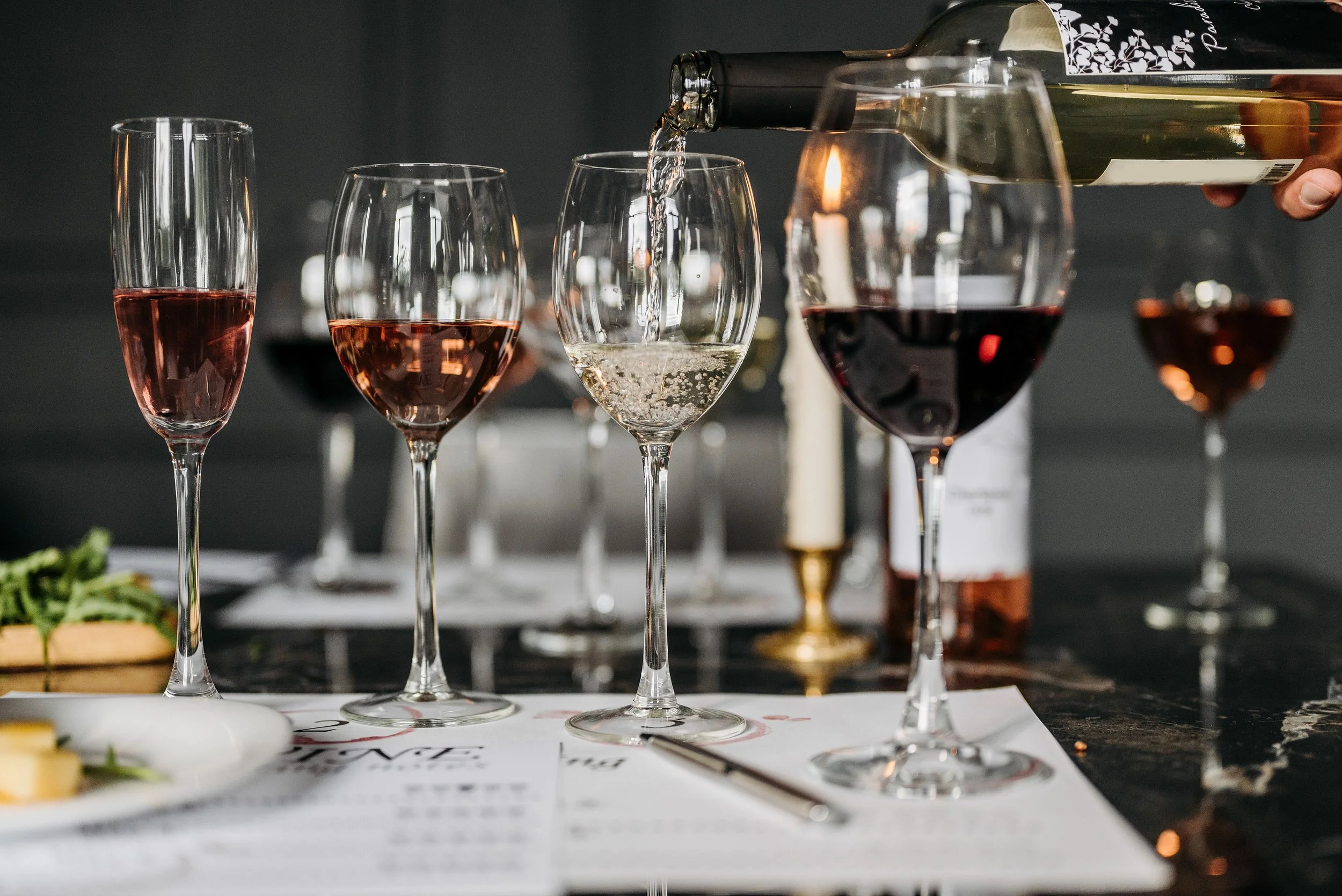 Pouring white wine into a glass at a wine tasting event with other wine glasses and bottles in the background.