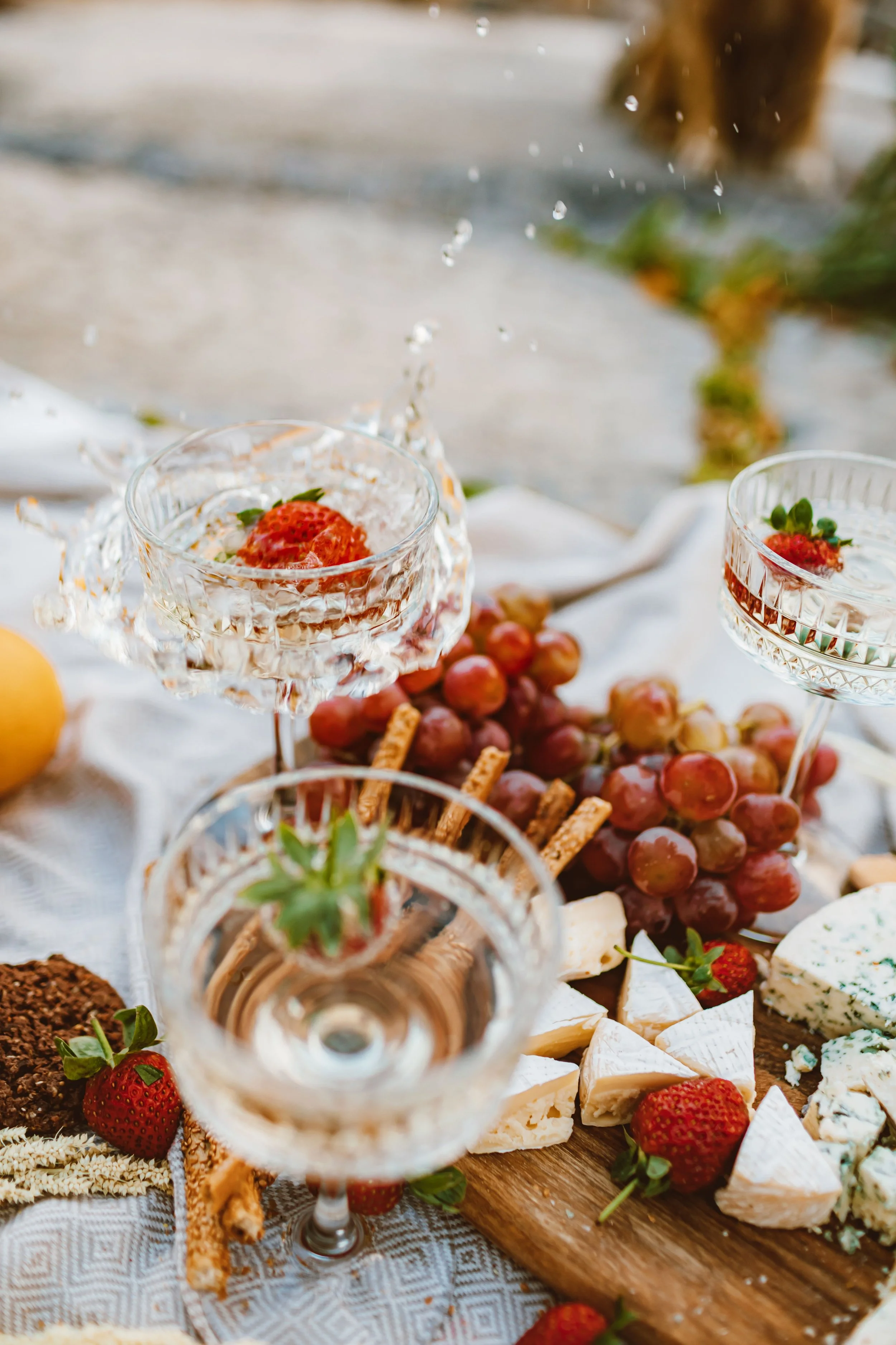 Close-up of a cheese and fruit platter with strawberries, grapes, and blue cheese, with empty crystal glasses in the foreground.