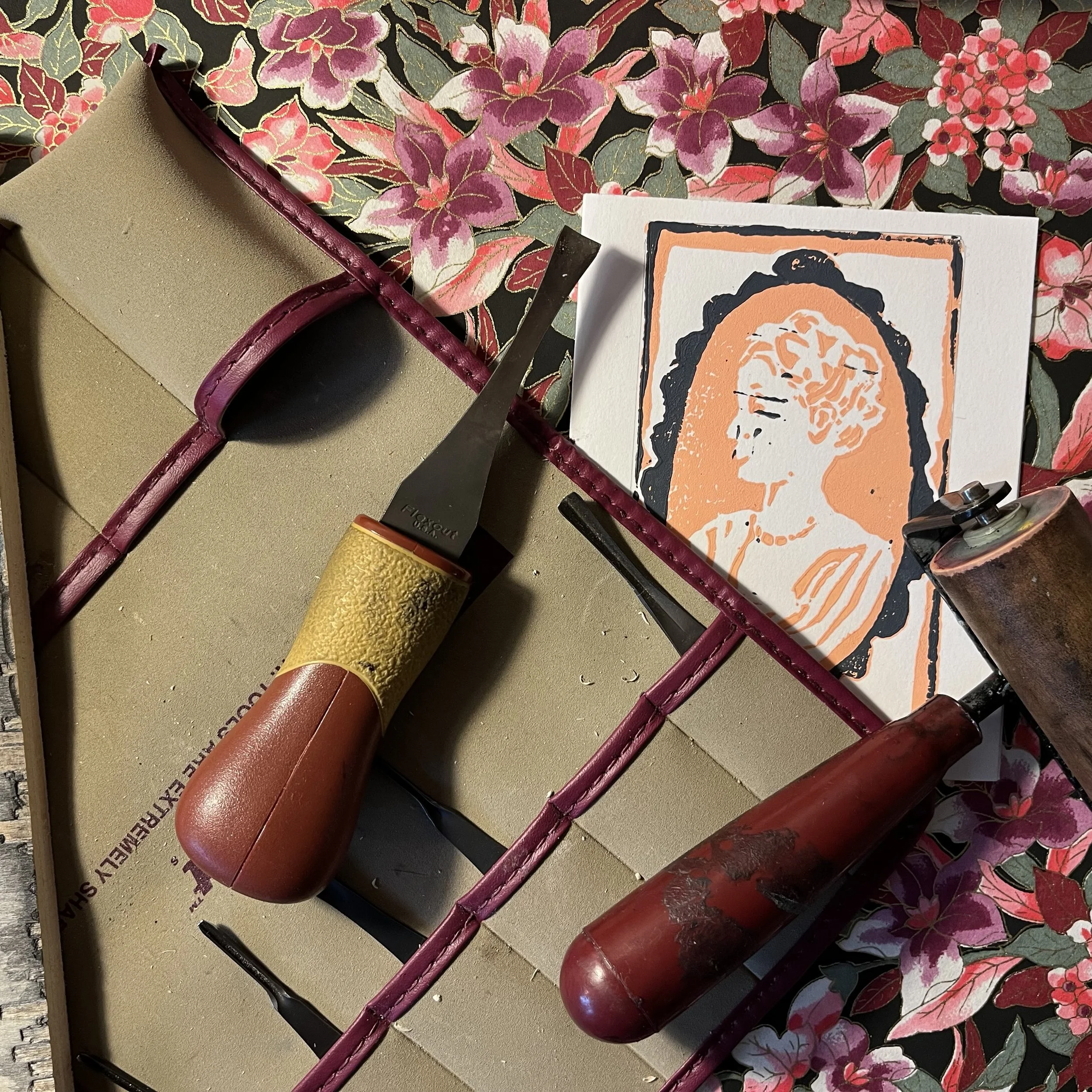 Image of a cameo style portrait in pink ink on white paper. carving tools seen overlapping print. background of image is a floral pattern (Copy)