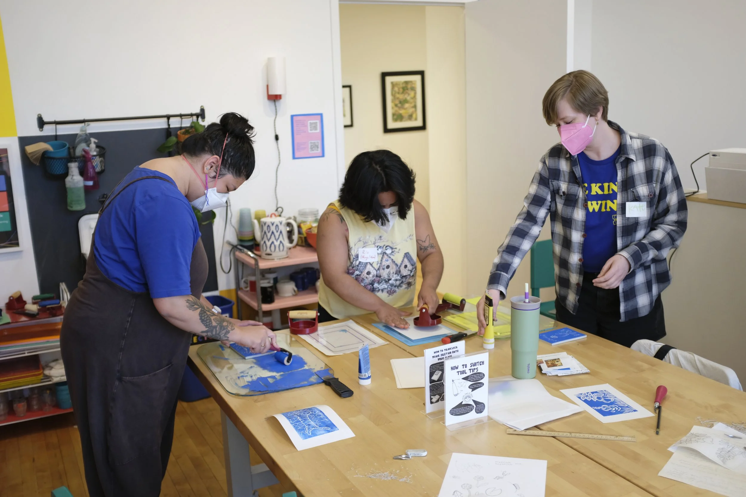 Masked participants standing around a table printing their relief carved blocks.