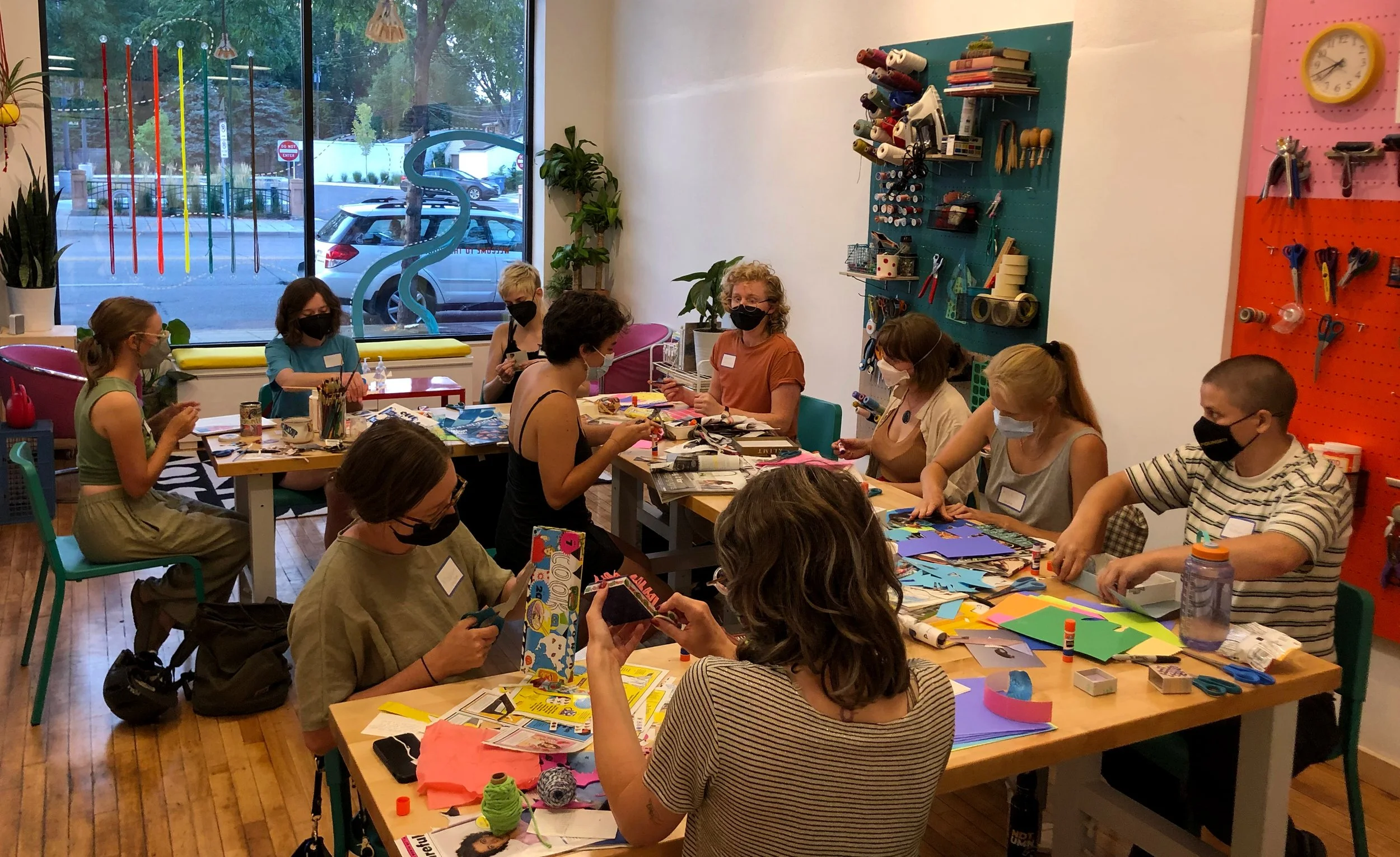 Group of 10 masked participants sat around a u-shaped table working on collages