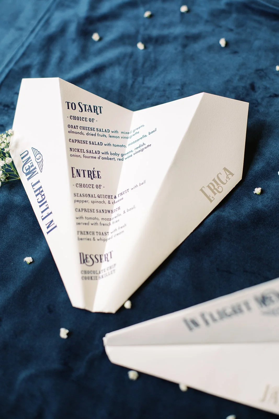 Paper airplane-inspired menus featuring modern typography in navy, light blue, and white, designed for a travel-themed baby shower celebration.