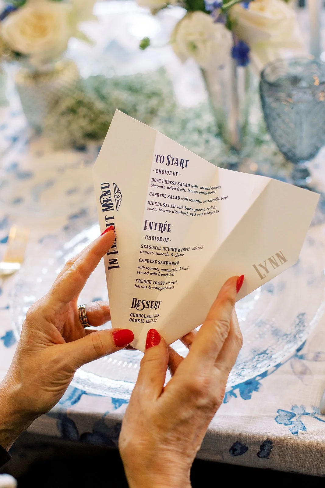 Paper airplane-inspired menus featuring modern typography in navy, light blue, and white, designed for a travel-themed baby shower celebration.