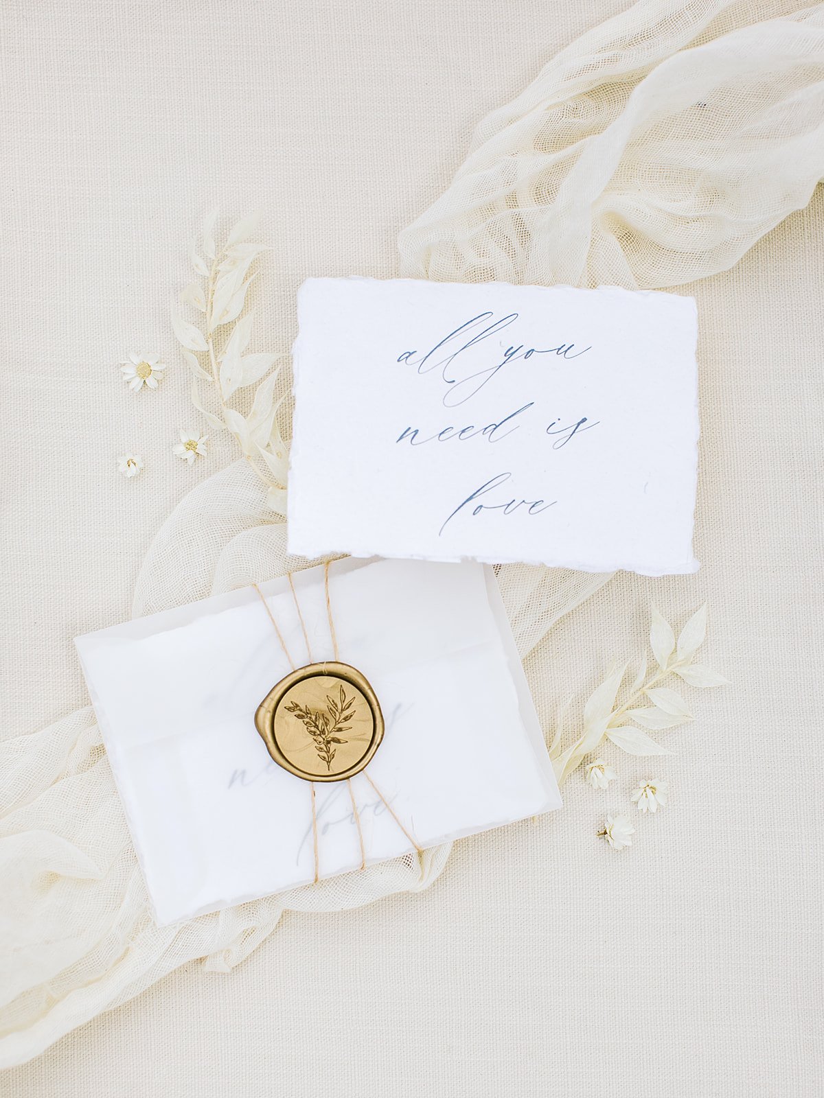 Handmade cotton paper wedding invitation with flowing calligraphy, a floral wax seal, and a delicate vellum envelope in a soft wildflower-inspired color palette.