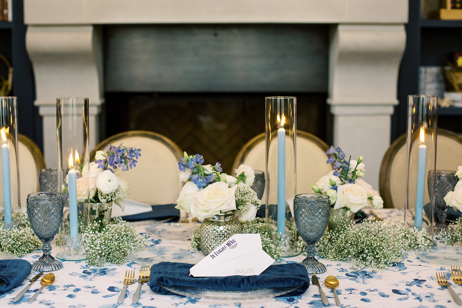 Baby shower place setting featuring a folded paper airplane menu, coordinated tableware, and travel-inspired details in navy, light blue, and white.