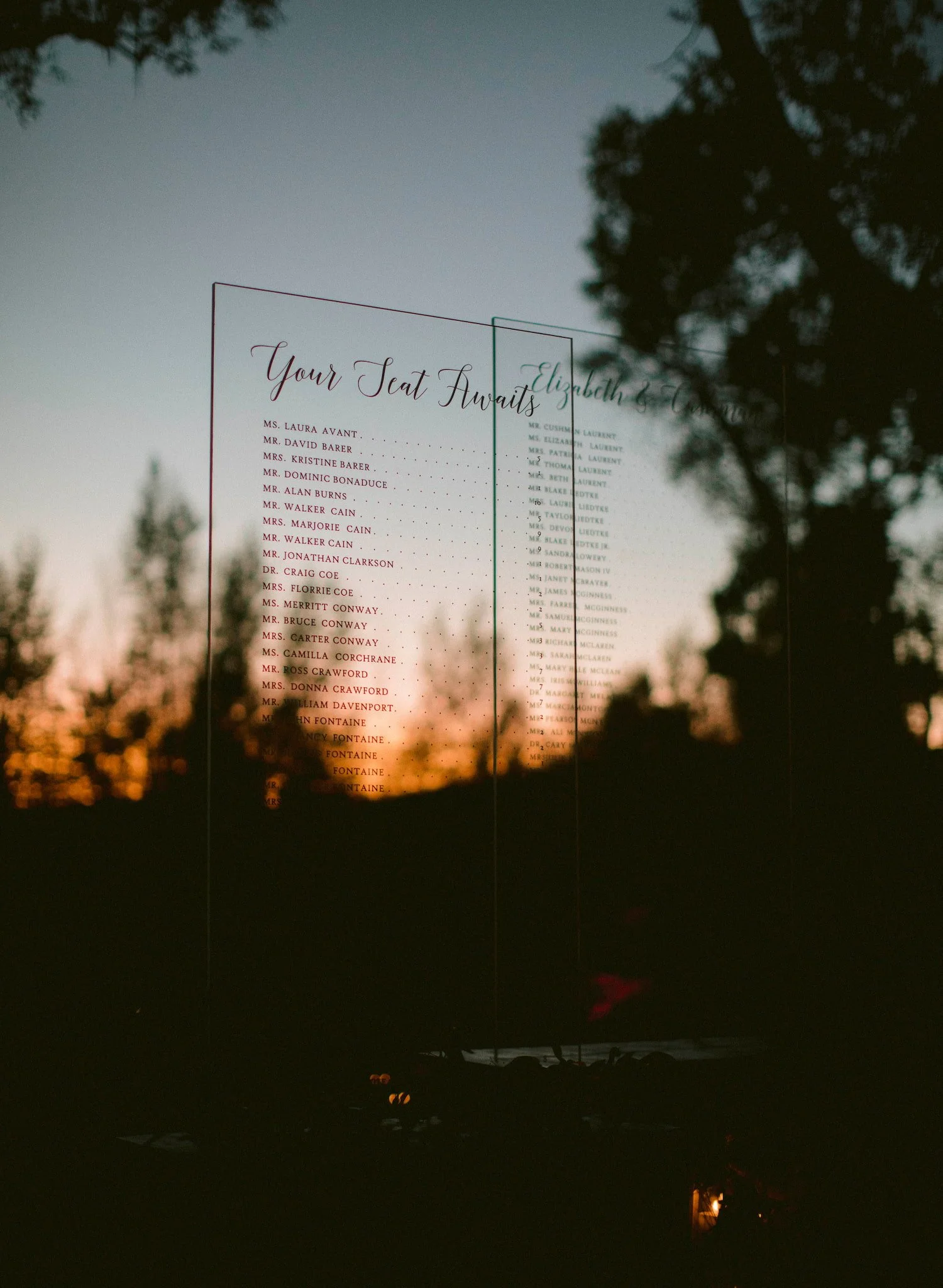 Custom acrylic seating chart displayed at the entrance to a grand floral archway leading guests into the wedding reception tent.