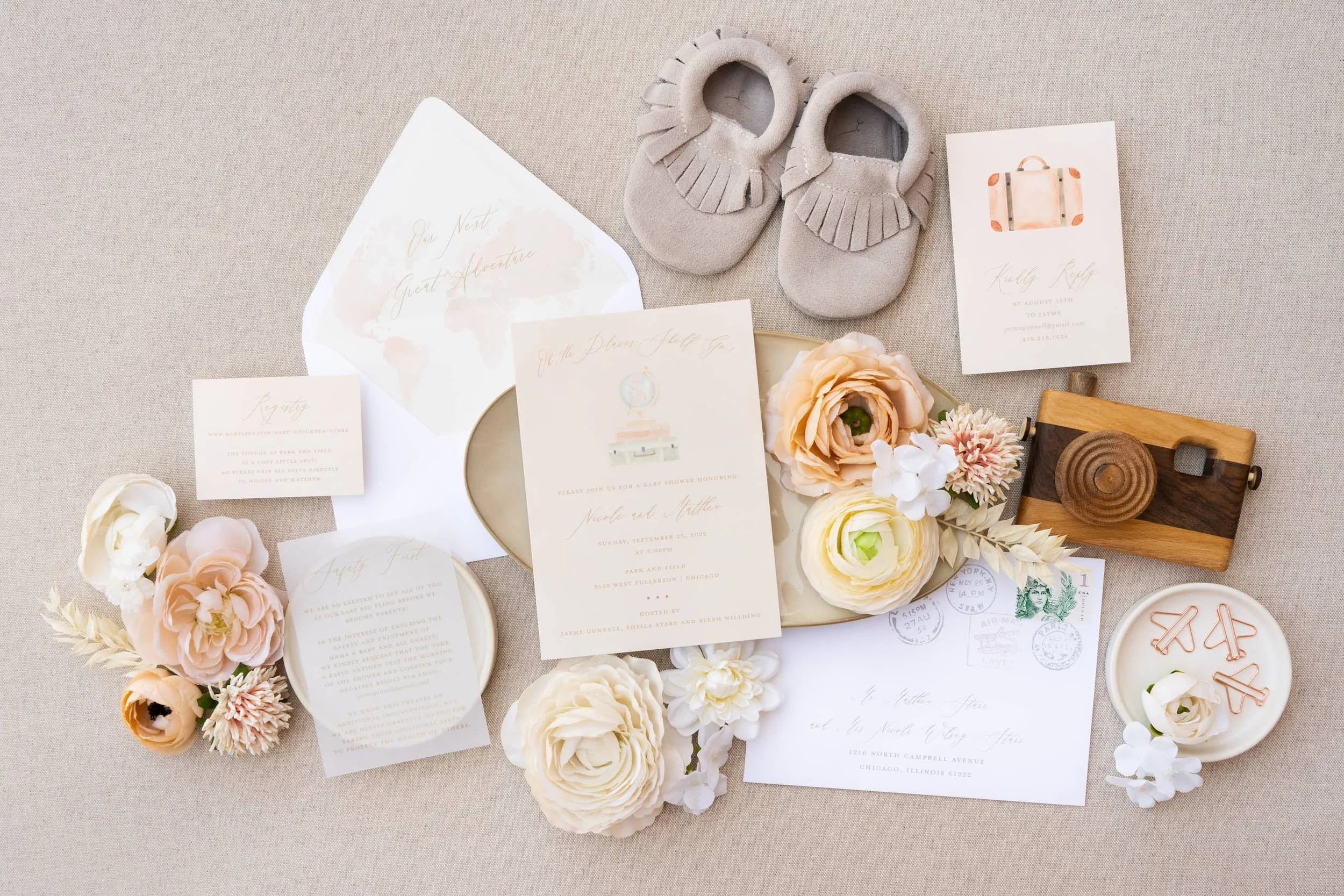 Flat lay of an adventure-themed baby shower invitation suite featuring peach and sage watercolor artwork, airplane paper clips, and travel-inspired stationery for a couple celebrating their next great adventure—welcoming a new baby.