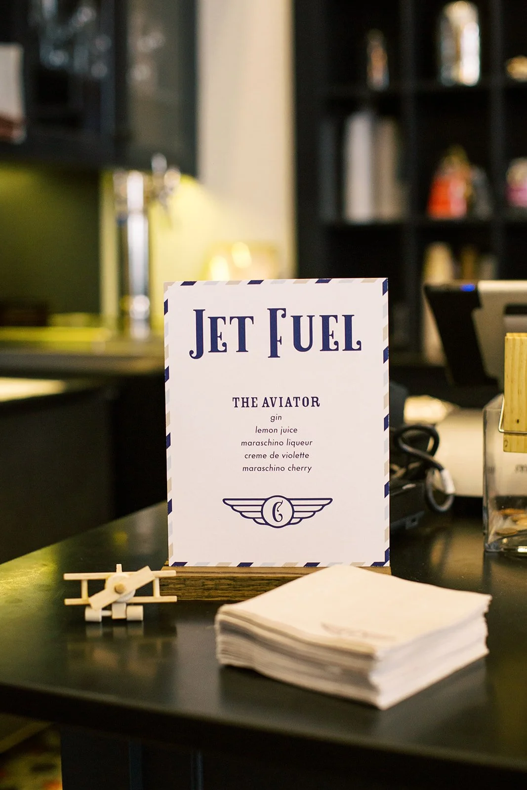 Travel-themed "Jet Fuel" bar sign paired with custom cocktail napkins and drink stir sticks, designed for an airplane-inspired baby shower celebration.