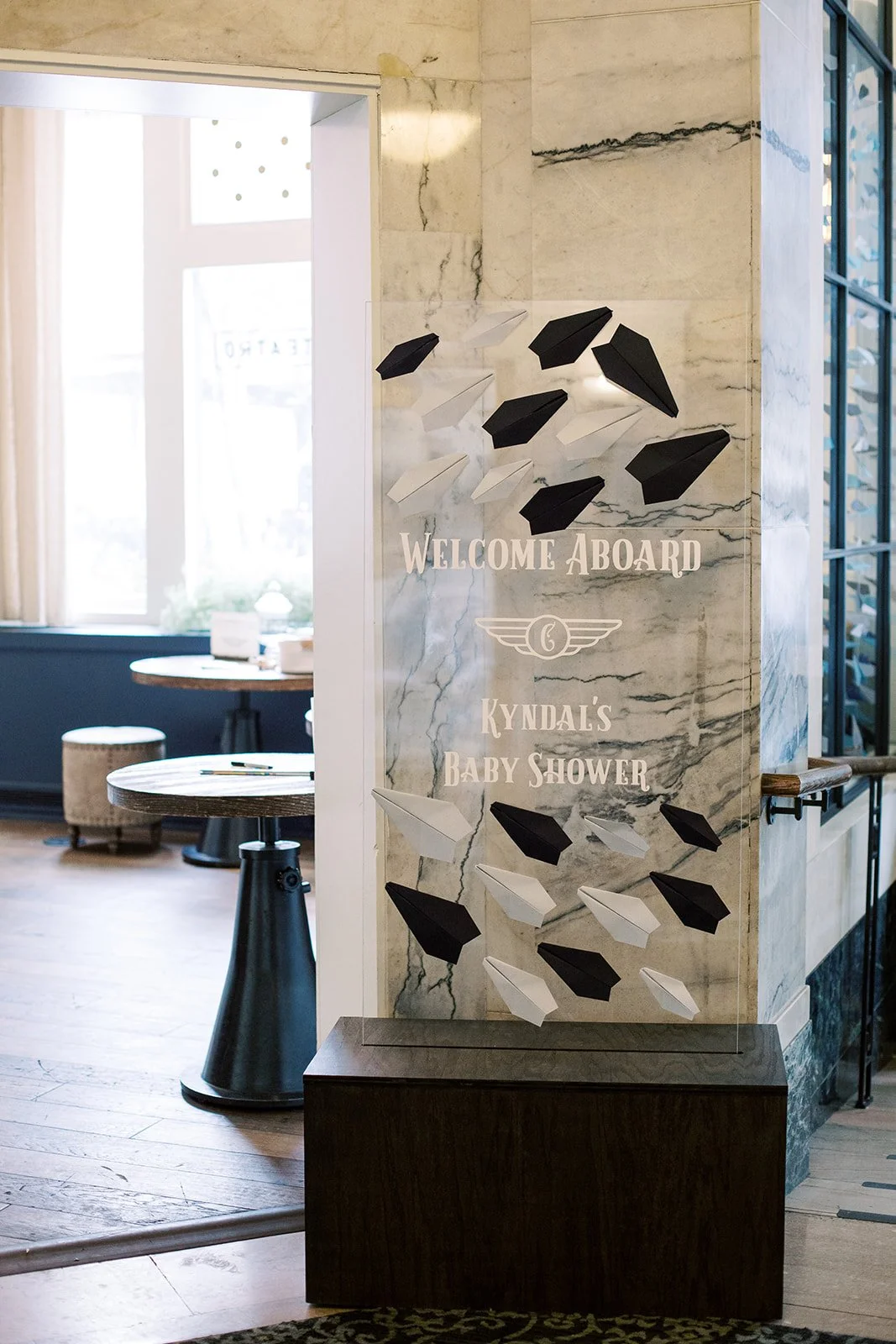 Travel-themed baby shower welcome sign featuring paper airplane illustrations in navy, light blue, and white, designed to greet guests at Hotel Teatro in Denver.