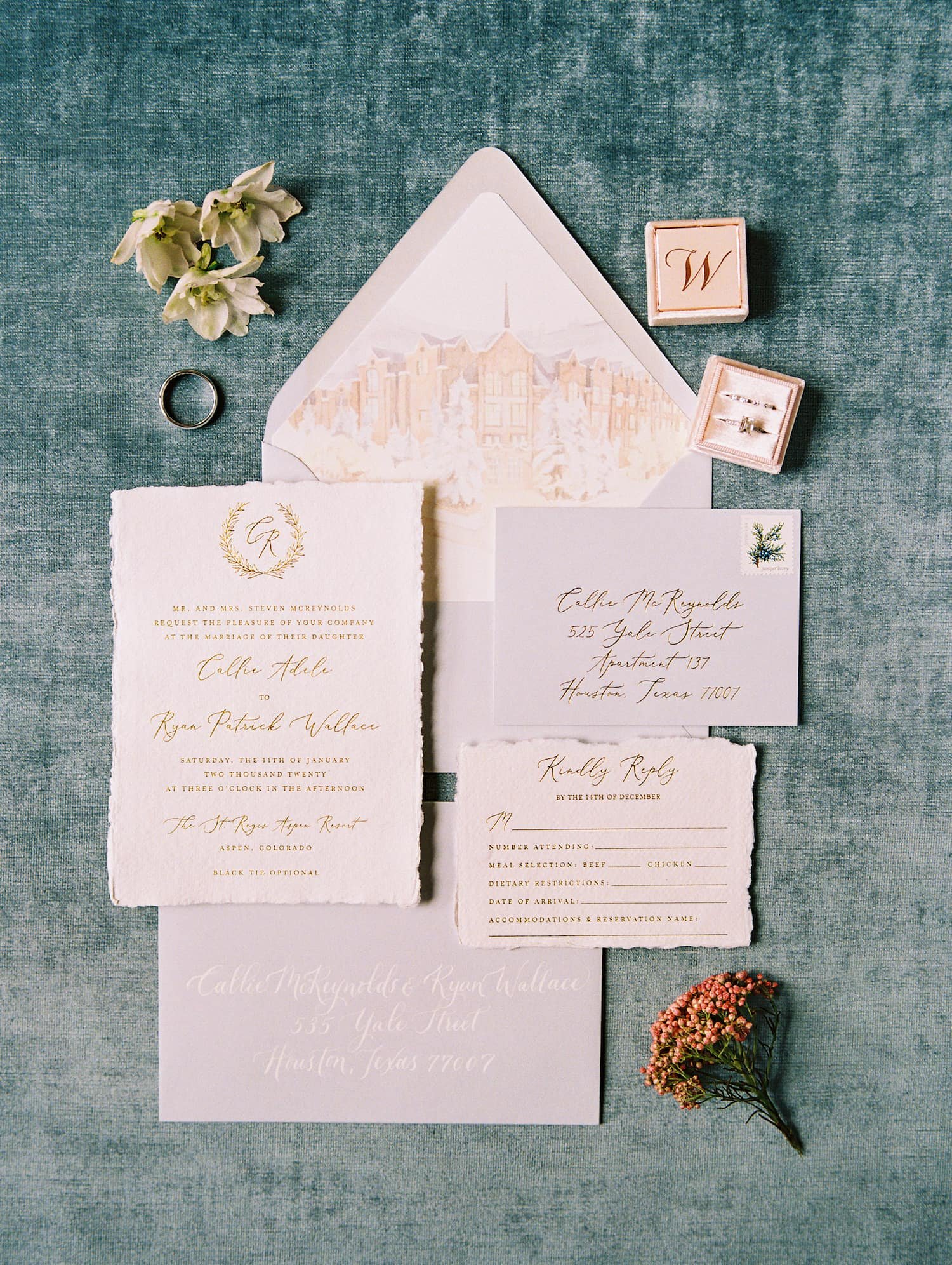 Flat lay of a luxury Aspen winter wedding invitation suite featuring handmade cotton paper with gold foil, steel blue details, silk ribbon, winter flora postage, and a custom watercolor envelope liner inspired by the Colorado mountains.