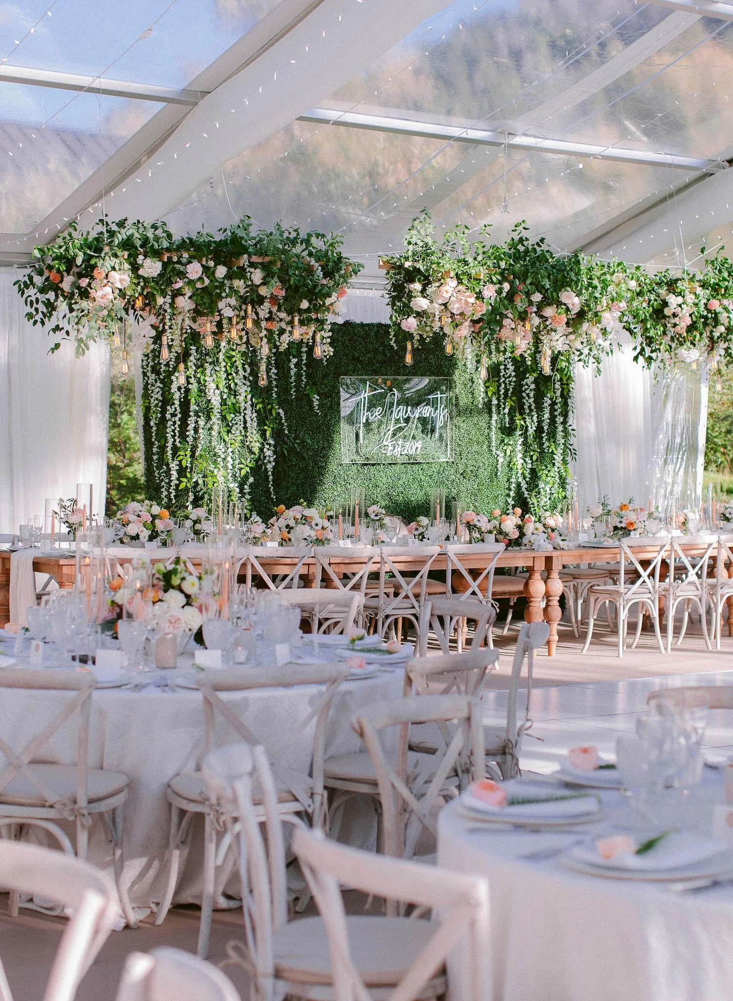 Reception stationery including menus, place cards, table numbers, and signature cocktail signs displayed beneath abundant floral arrangements in a luxury reception tent.