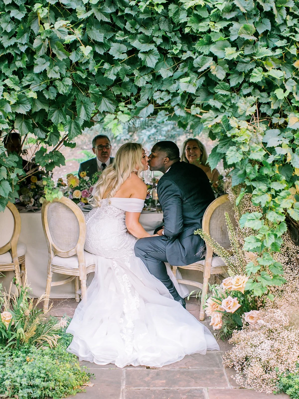Bride and groom in vine covered dinner spot at long beautiful table for wedding at Boulder Flower Farm