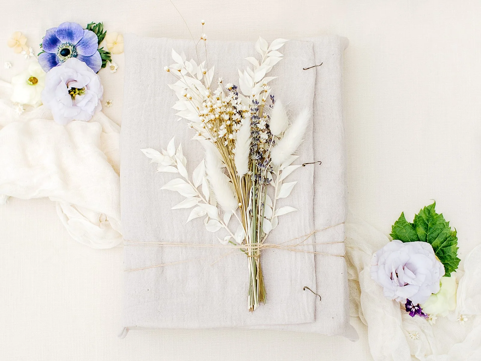 Close-up of hand-dyed silk, cotton gauze, antique brass clips, and locally sourced dried florals styled with handmade wedding stationery.