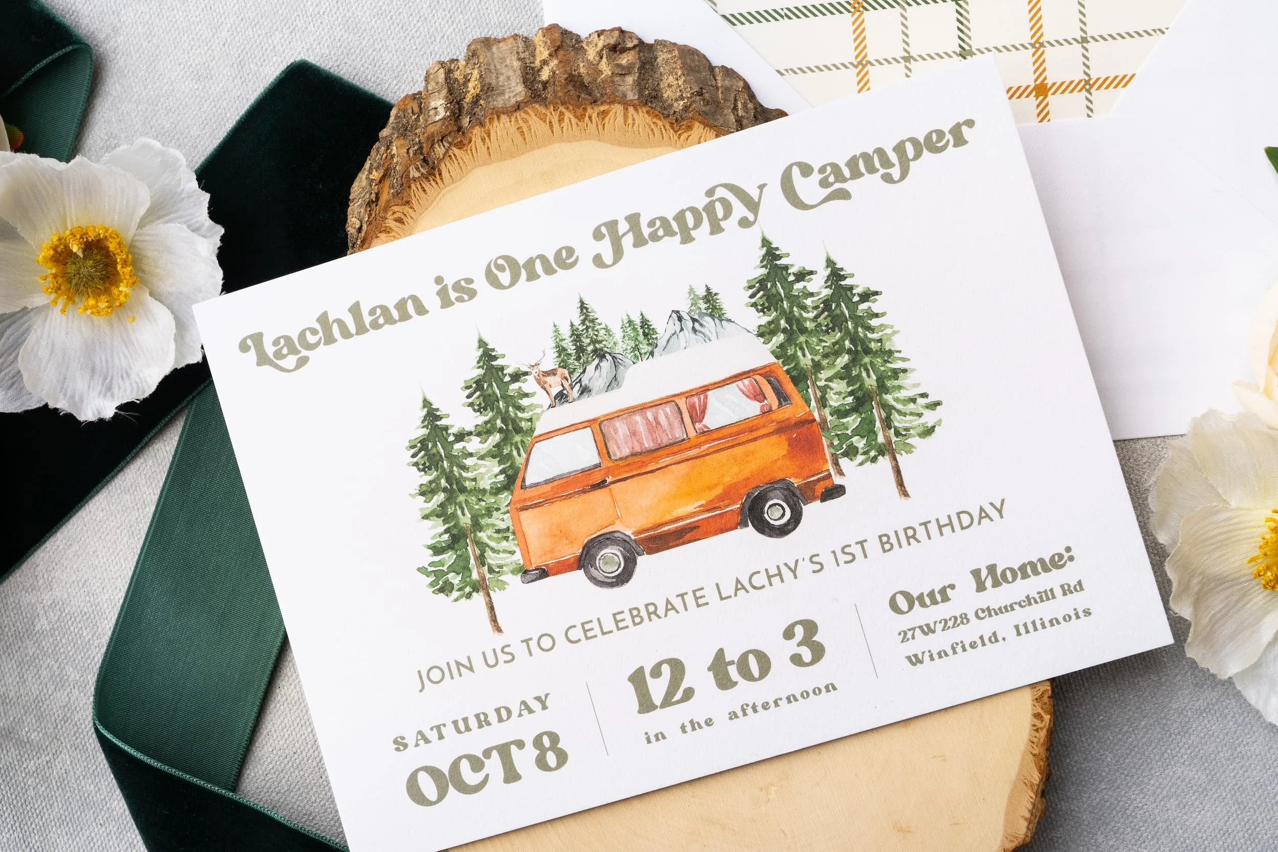 “One Happy Camper” first birthday invitation suite with plaid envelope liner, watercolor camping illustrations, die-cut campfire RSVP card, and green-and-white baker’s twine.