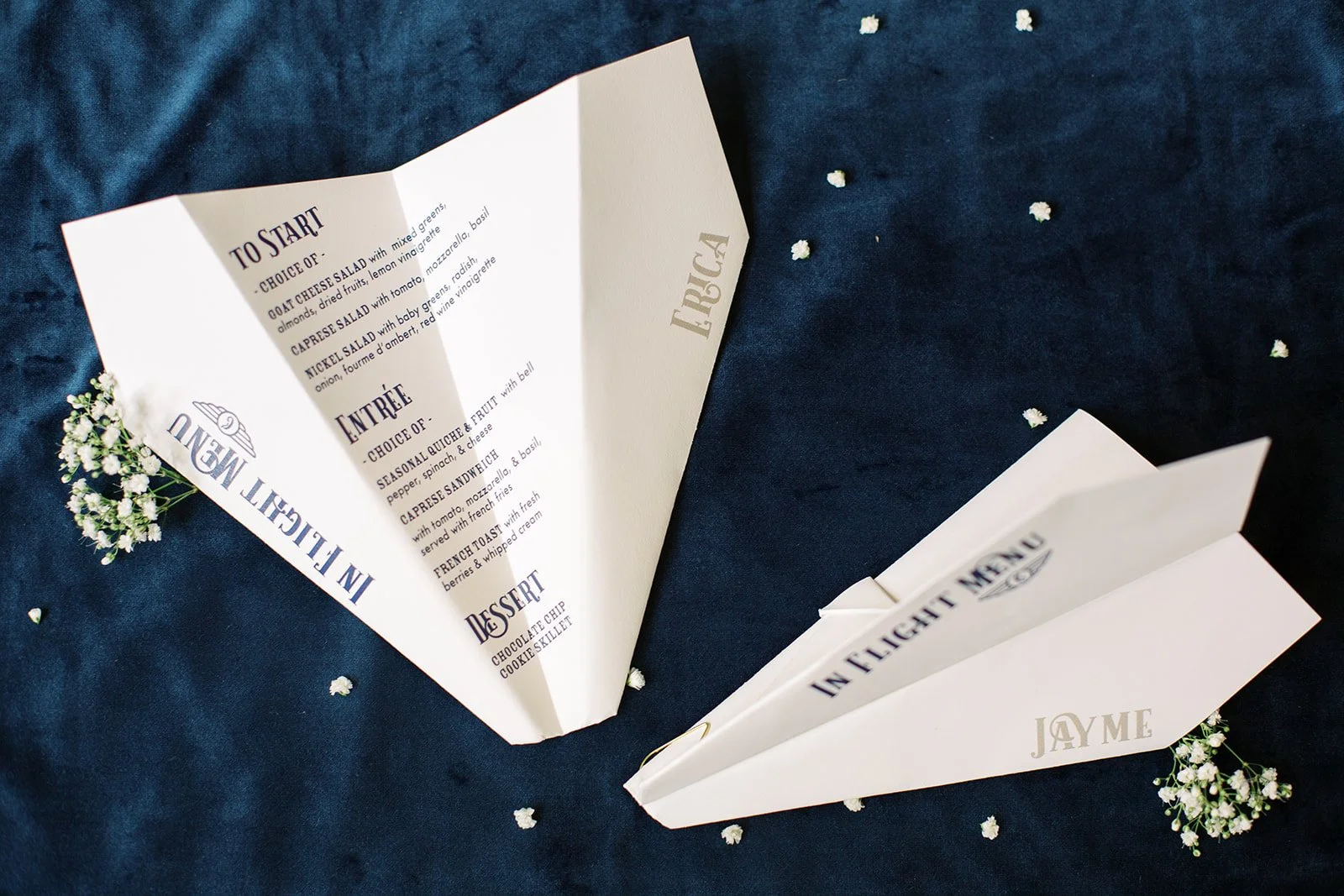 Paper airplane-inspired menus featuring modern typography in navy, light blue, and white, designed for a travel-themed baby shower celebration.
