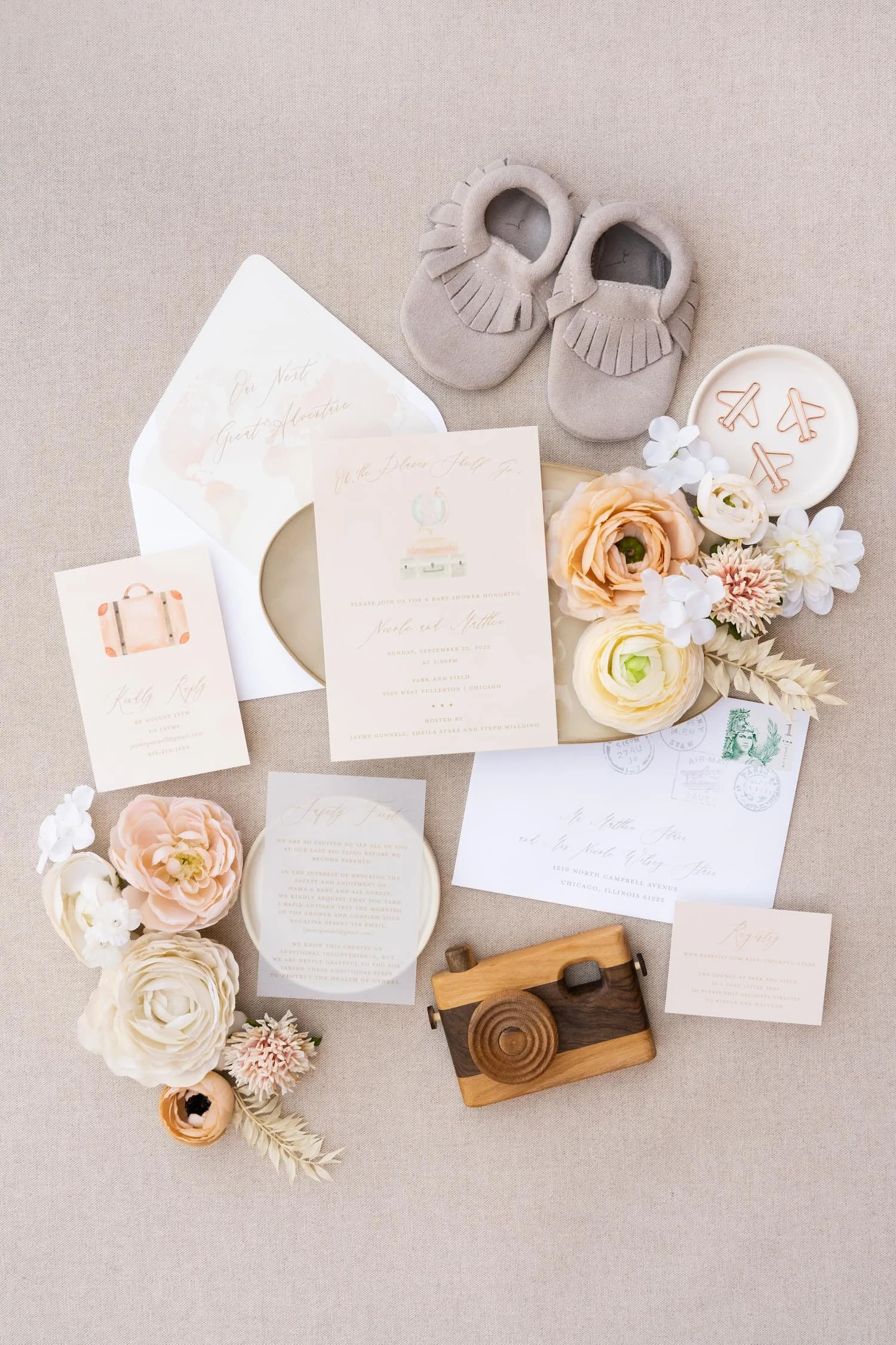 Flat lay of an adventure-themed baby shower invitation suite featuring peach and sage watercolor artwork, airplane paper clips, and travel-inspired stationery for a couple celebrating their next great adventure—welcoming a new baby.