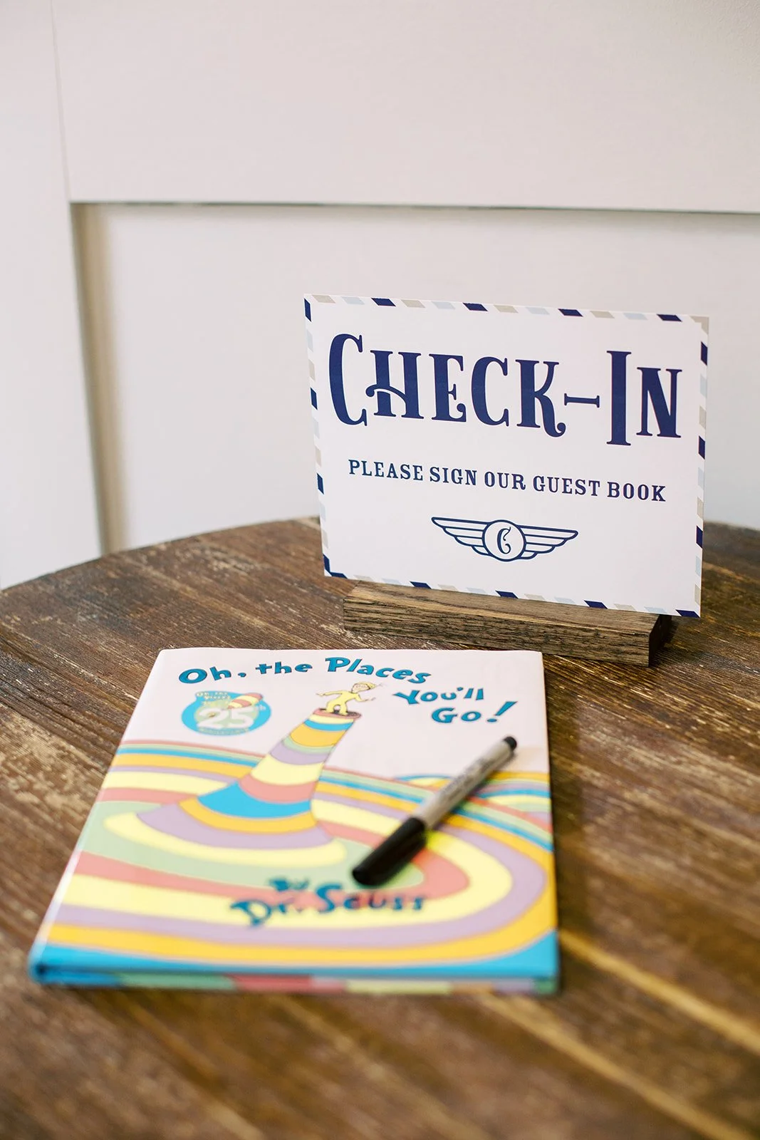 Baby shower guest book check-in featuring Oh, the Places You'll Go! by Dr. Seuss for guests to sign, styled as an airport-inspired check-in station celebrating the parents' love of travel.