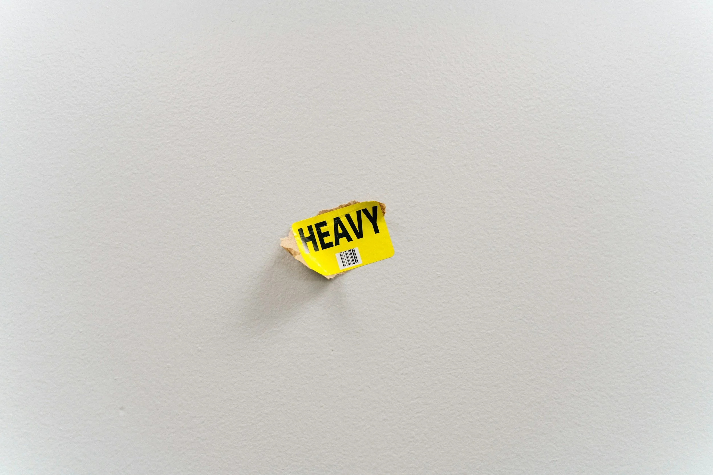 Yellow sticker saying "HEAVY" on white wall, representing heaviness of current political climate