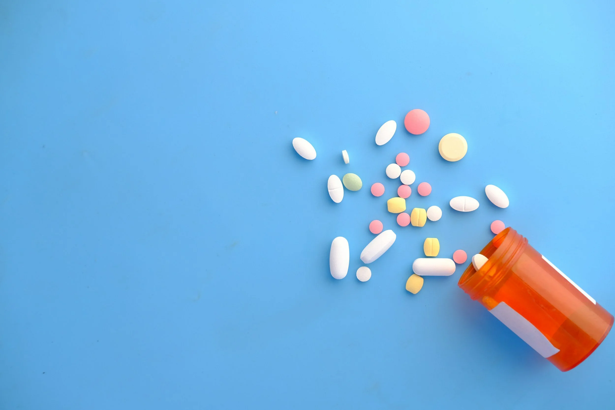 assortment of colorful pills spilling out of pill bottle on blue background