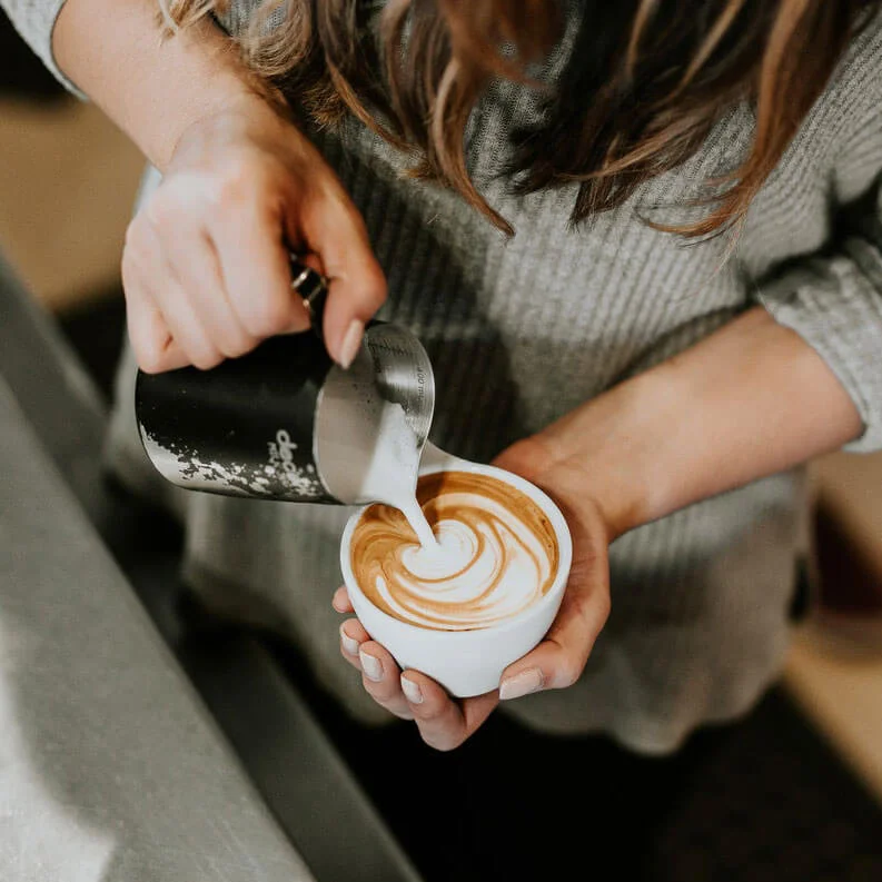barista pouring hot milk into a coffee cup to make a flat white coffee