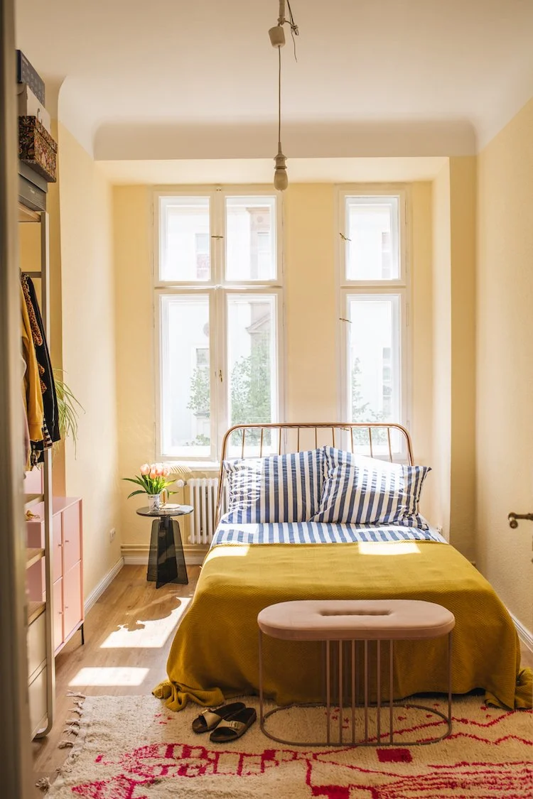    a colourful bright apartment in berlin, gallery wall, artworks, pink kitchen, terrazzo worktops, terrazzo, striped bedclothes, bedroom, striped curtains, seating area, curtains, stipes, yellow sofa, living room, large living room windows, balcony 