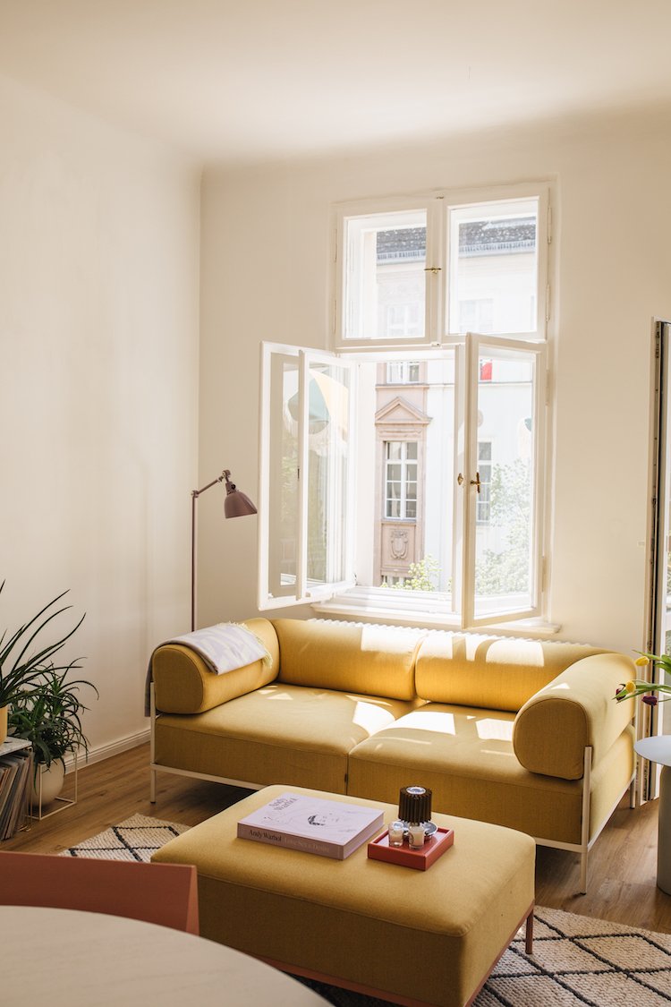    a colourful bright apartment in berlin, gallery wall, artworks, pink kitchen, terrazzo worktops, terrazzo, striped bedclothes, bedroom, striped curtains, seating area, curtains, stipes, yellow sofa, living room, large living room windows, balcony 