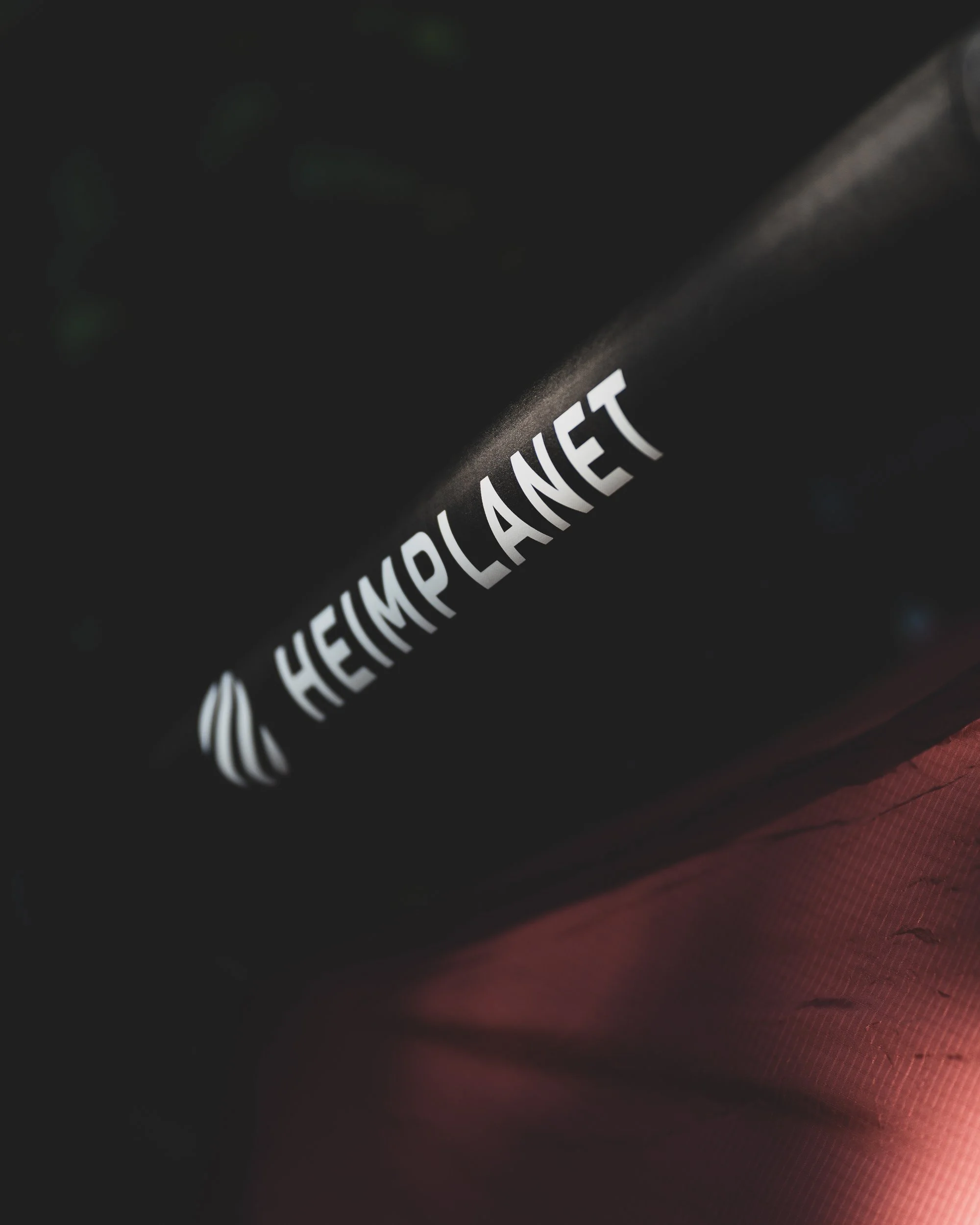 Close-up of a product label with the text 'Hemp Planet' in white on a black background, partially illuminated, with a dark and textured surface in the background.