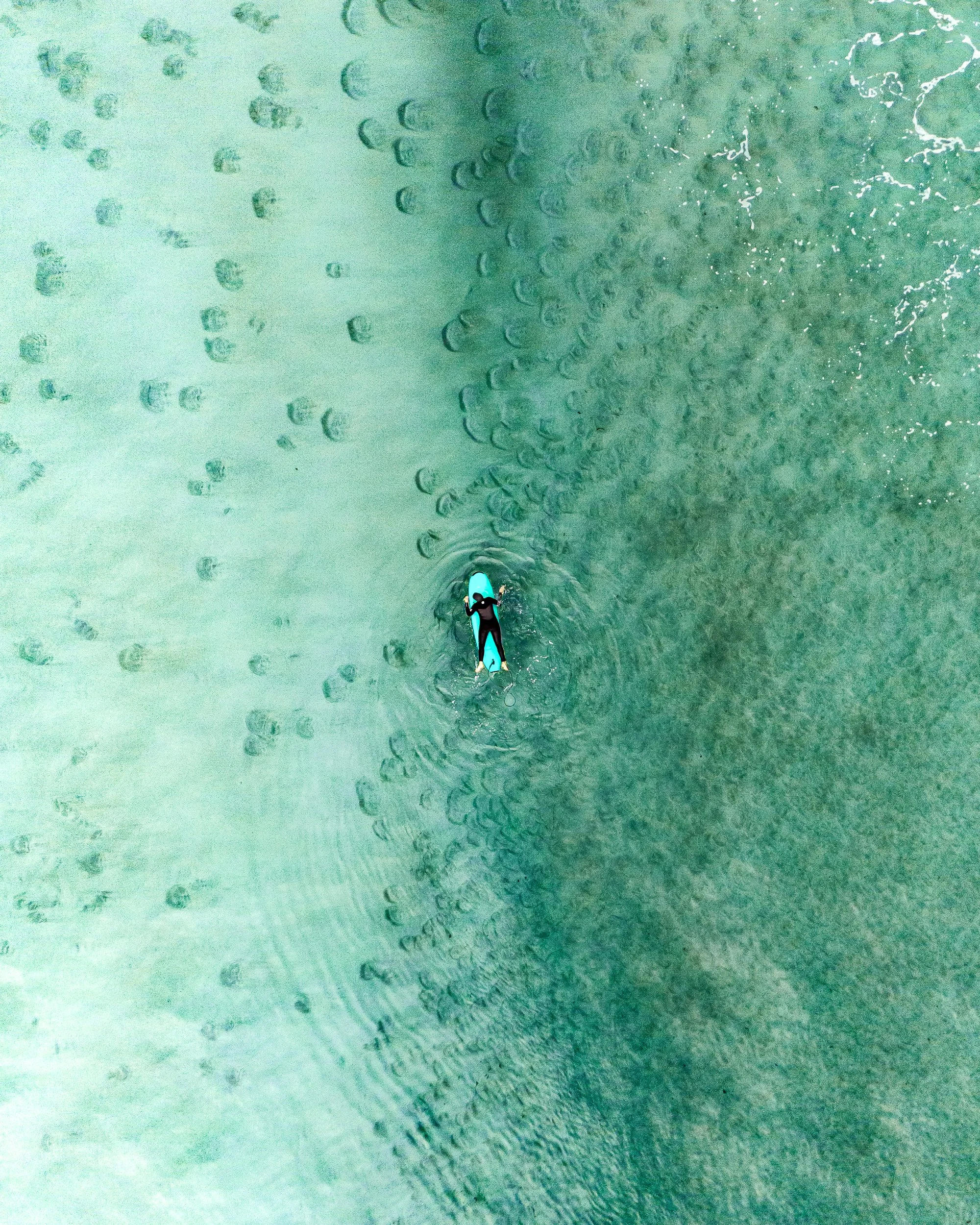 An aerial view of a person paddleboarding on the water, leaving a trail of ripples behind.