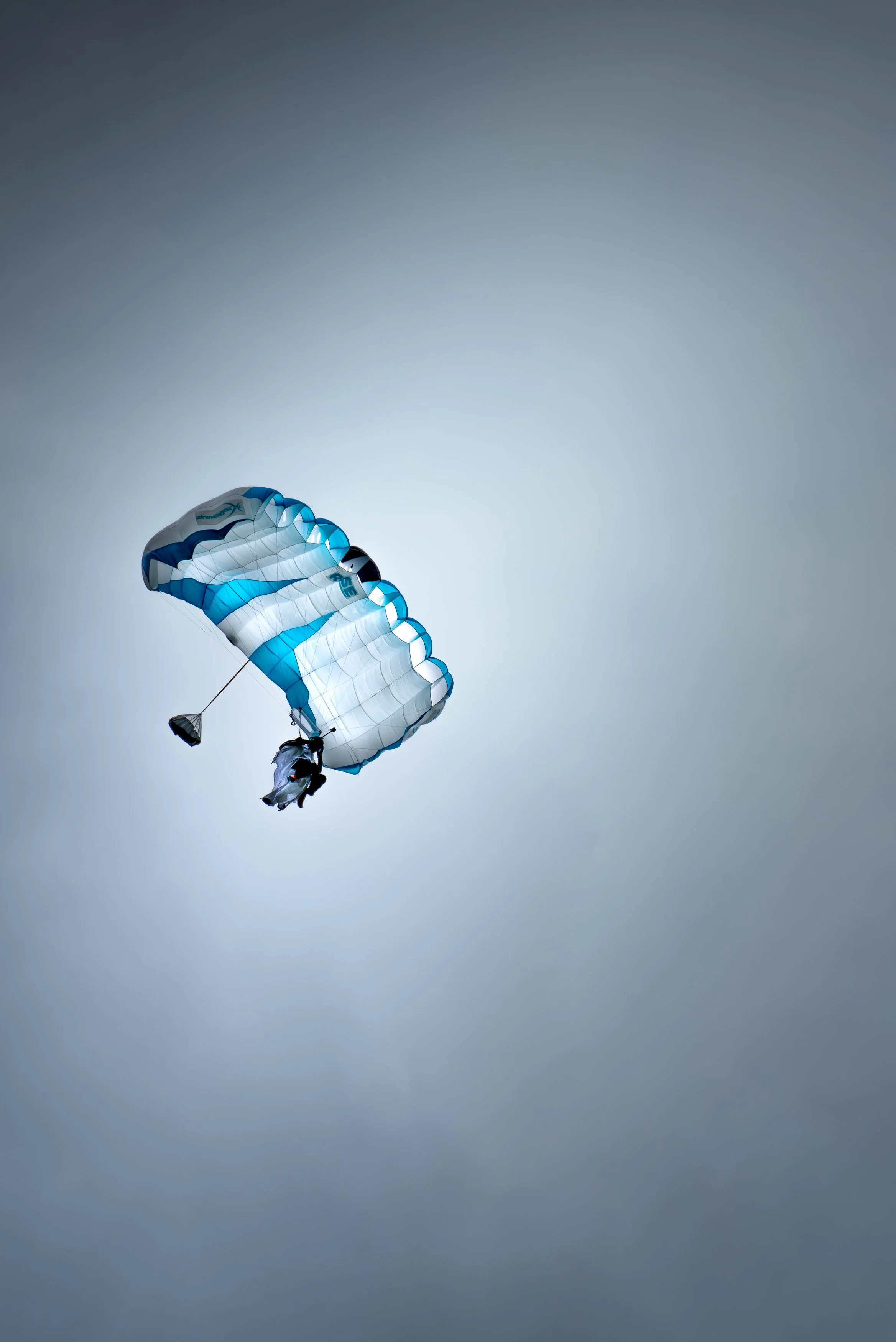 Person paragliding with a blue and white canopy in the sky.