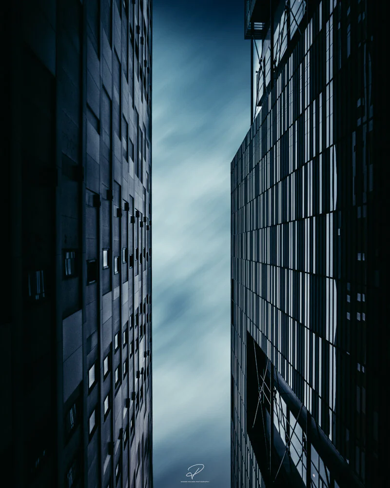 Looking up between two tall modern office buildings with glass and metal facades, reaching towards a cloudy sky. Arkitektur foto Oslo.